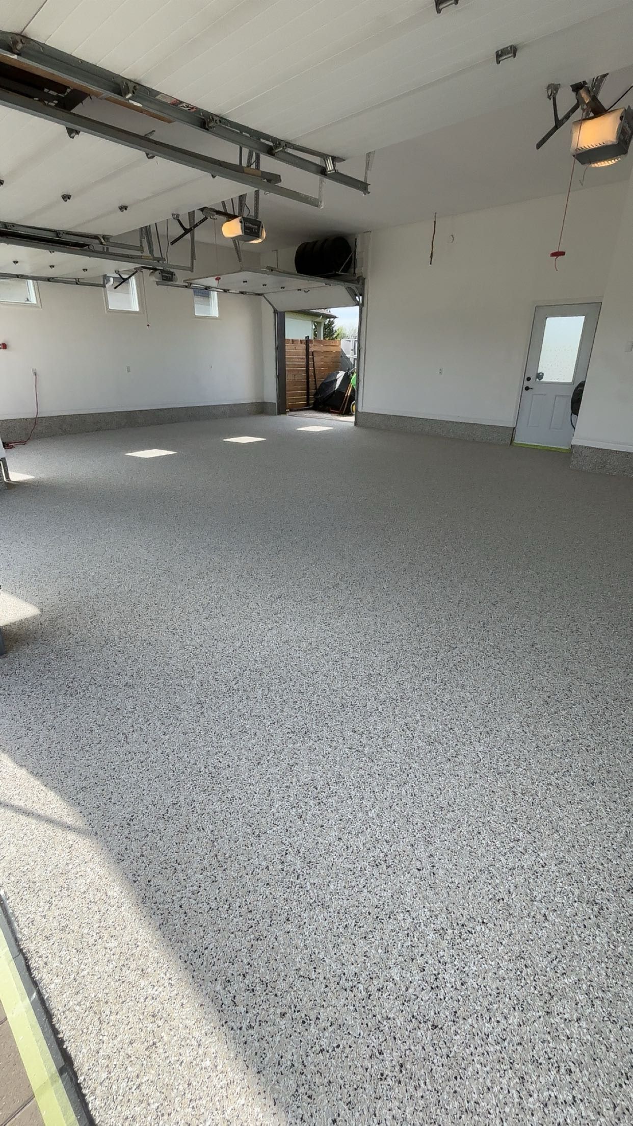 Empty garage interior with gray floor, white walls, overhead lights, and an open doorway in the back