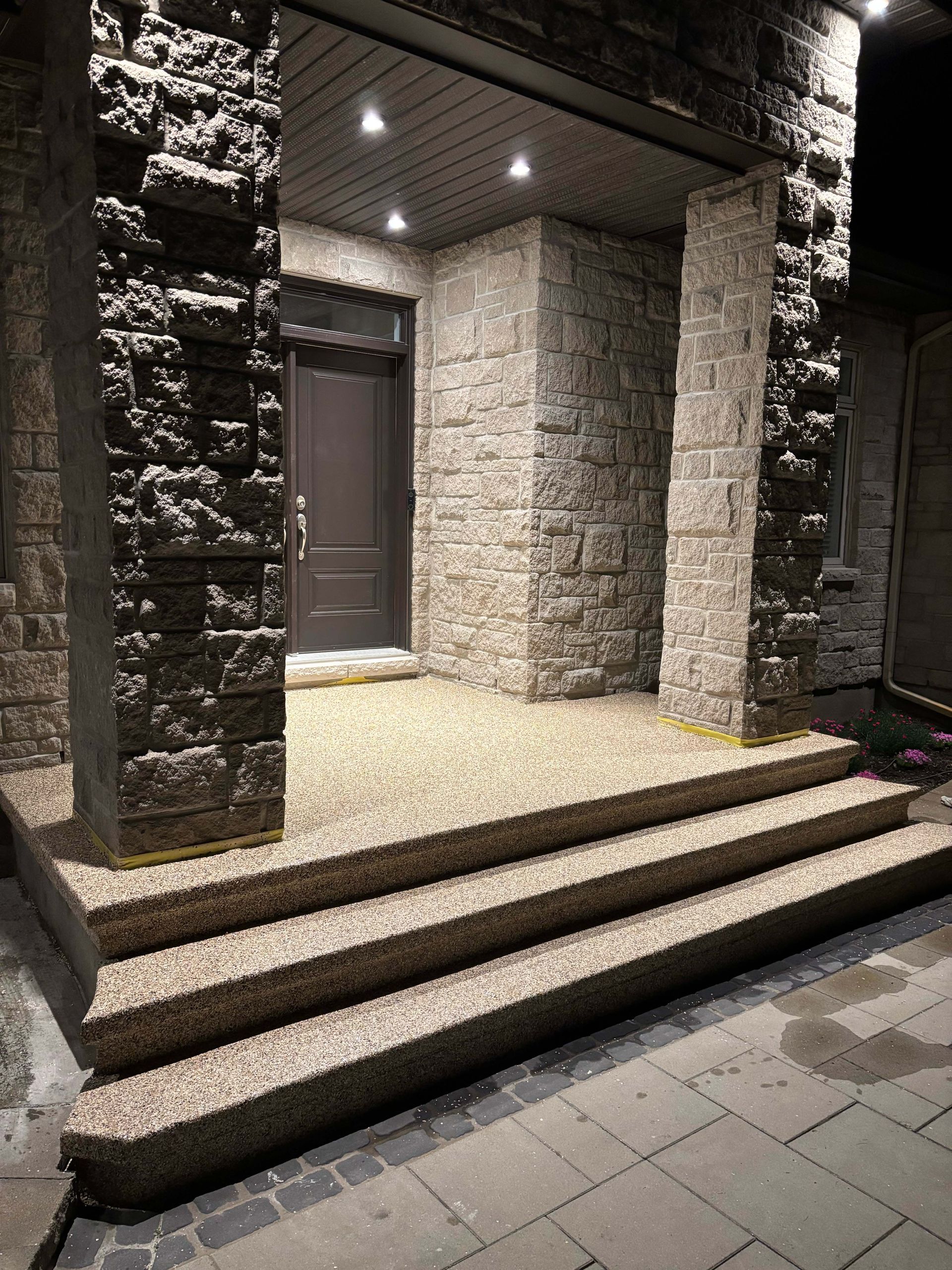 Stone apartment entrance with lit steps, a dark door, and textured columns at night