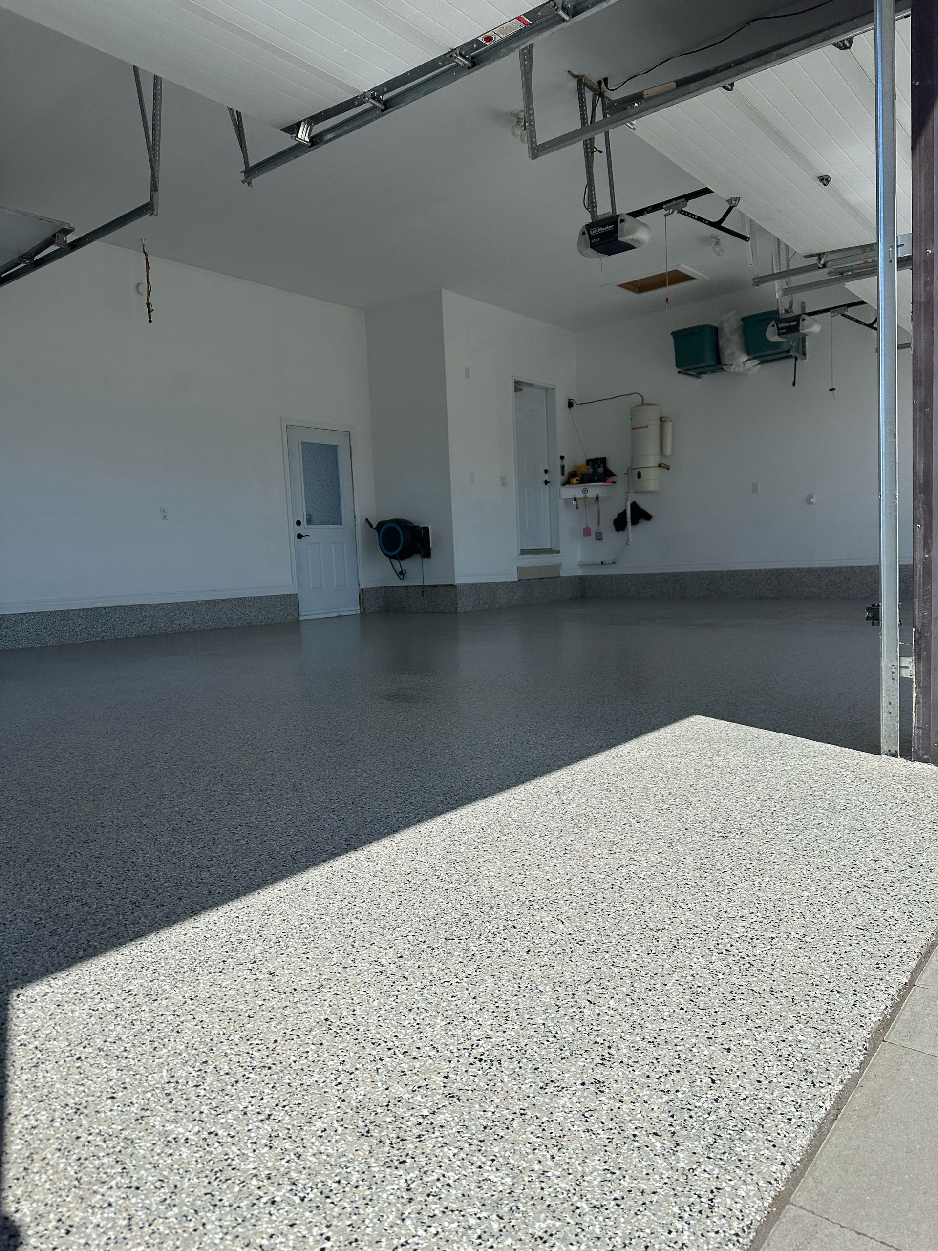Empty garage interior with white walls, speckled floor, and overhead door tracks visible