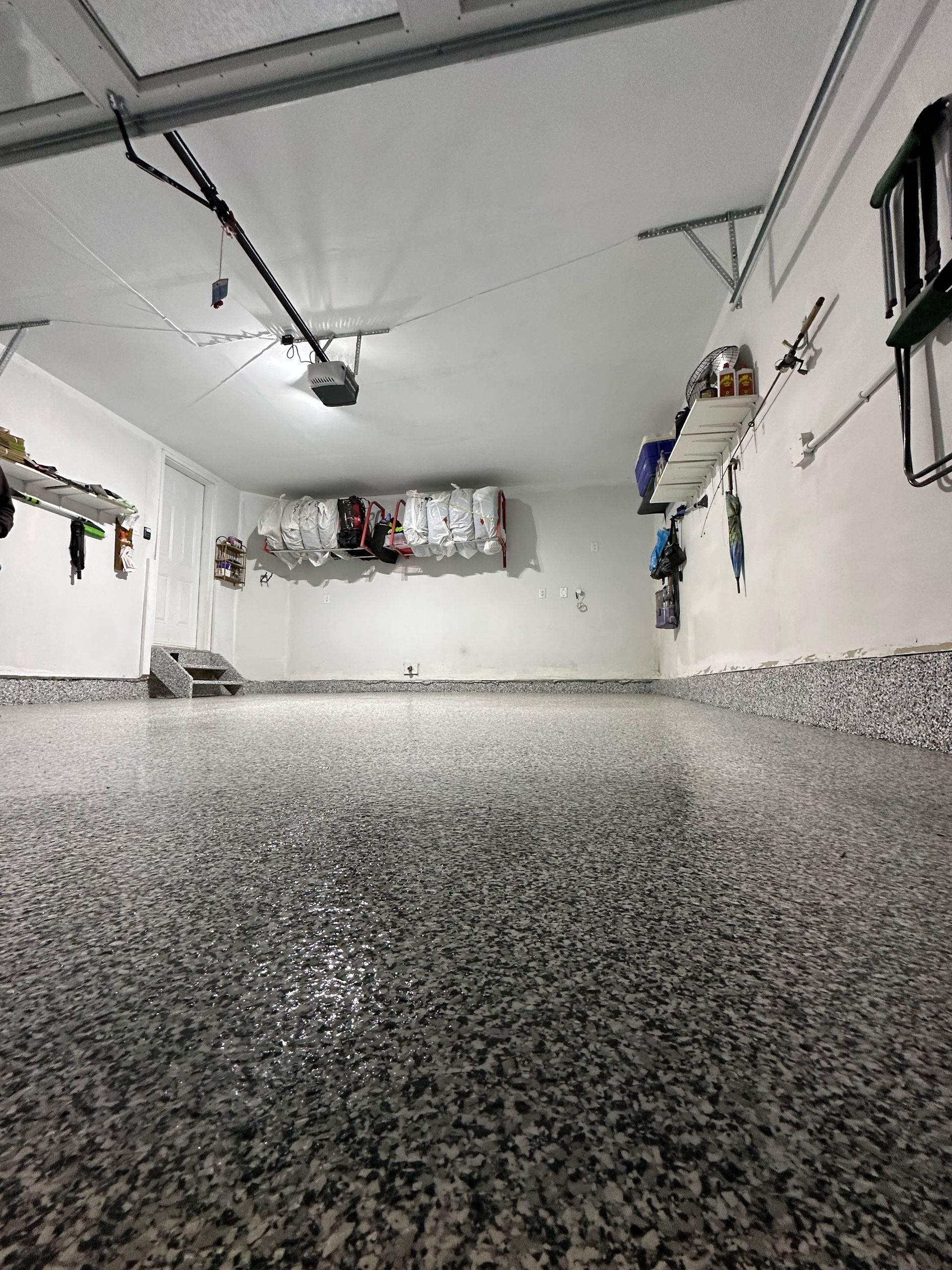 Empty garage with speckled epoxy floor, white walls, ceiling lights, and shelves along the sides