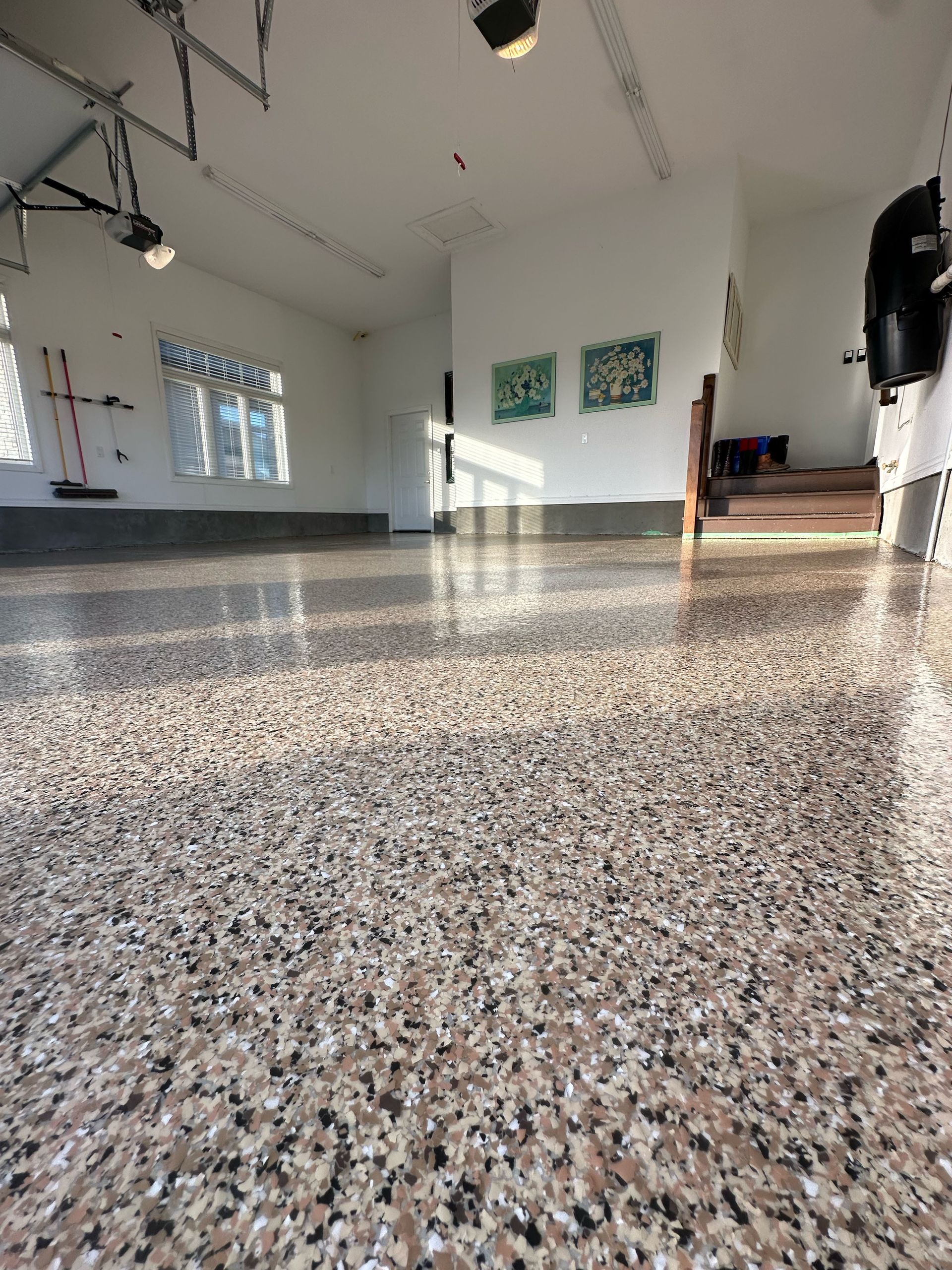 Empty gallery room with polished speckled floor, white walls, and sunlight streaming in through windows.