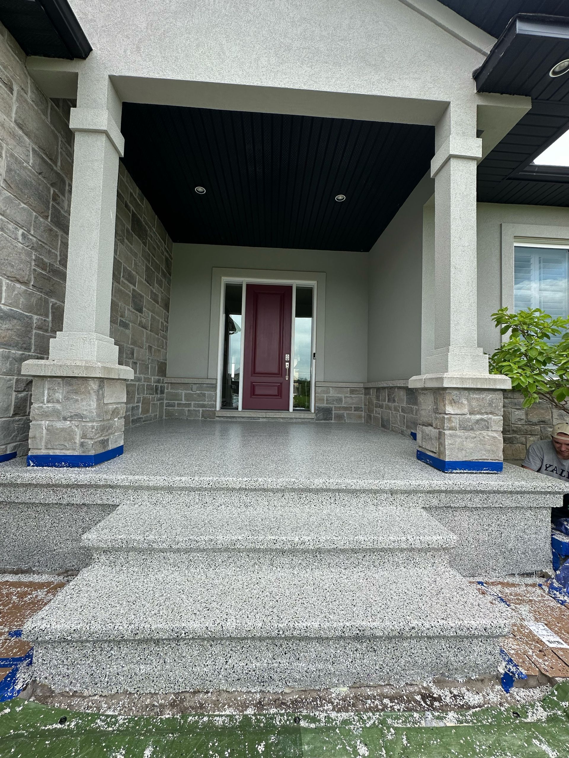 Front porch with stone steps, white columns, and a red front door under a covered entry.