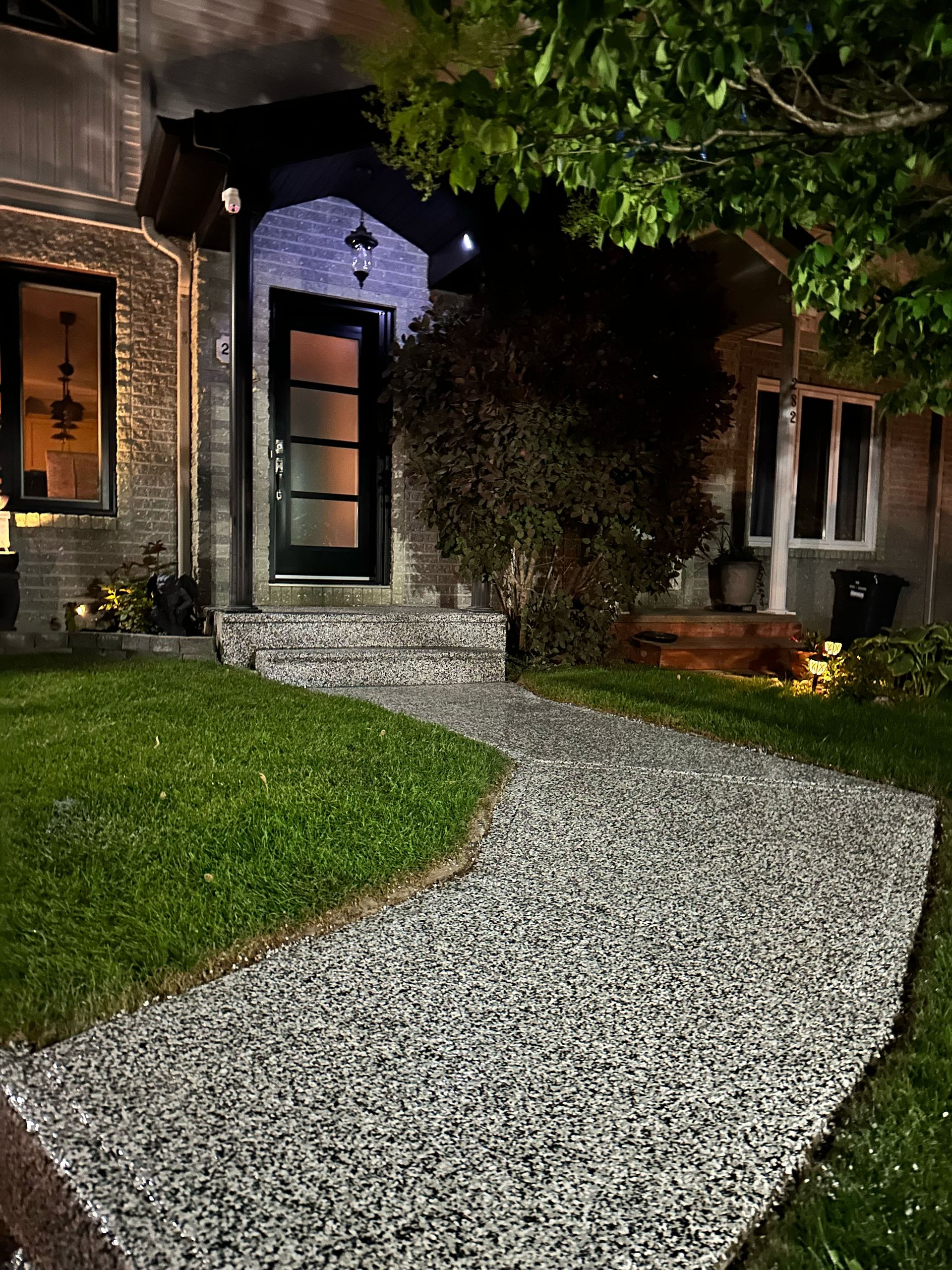 Nighttime front yard with a curved gravel path leading to a lit house entrance and windows.