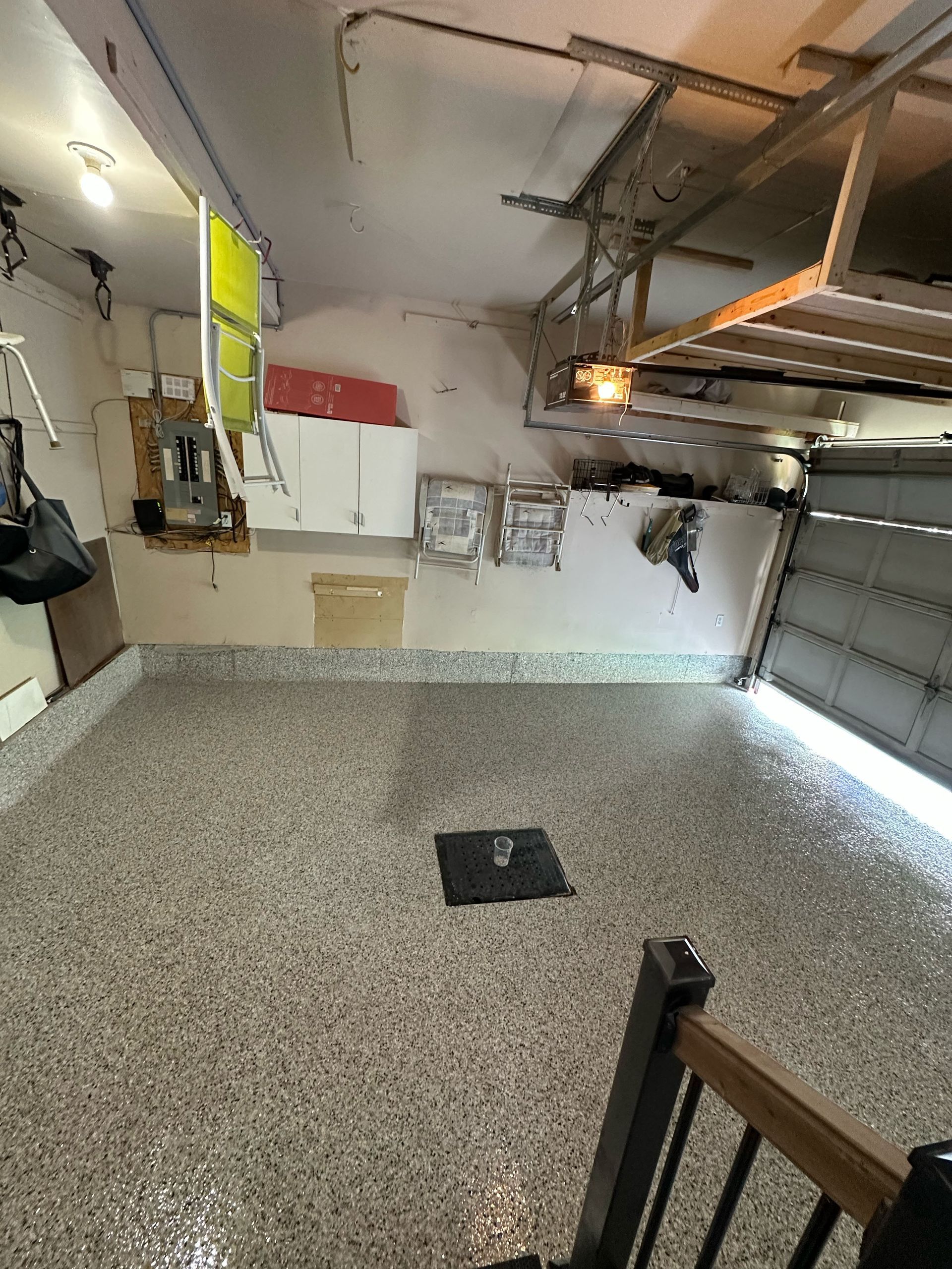 Empty garage with speckled floor, overhead opener, wall cabinets, and a partially open garage door.