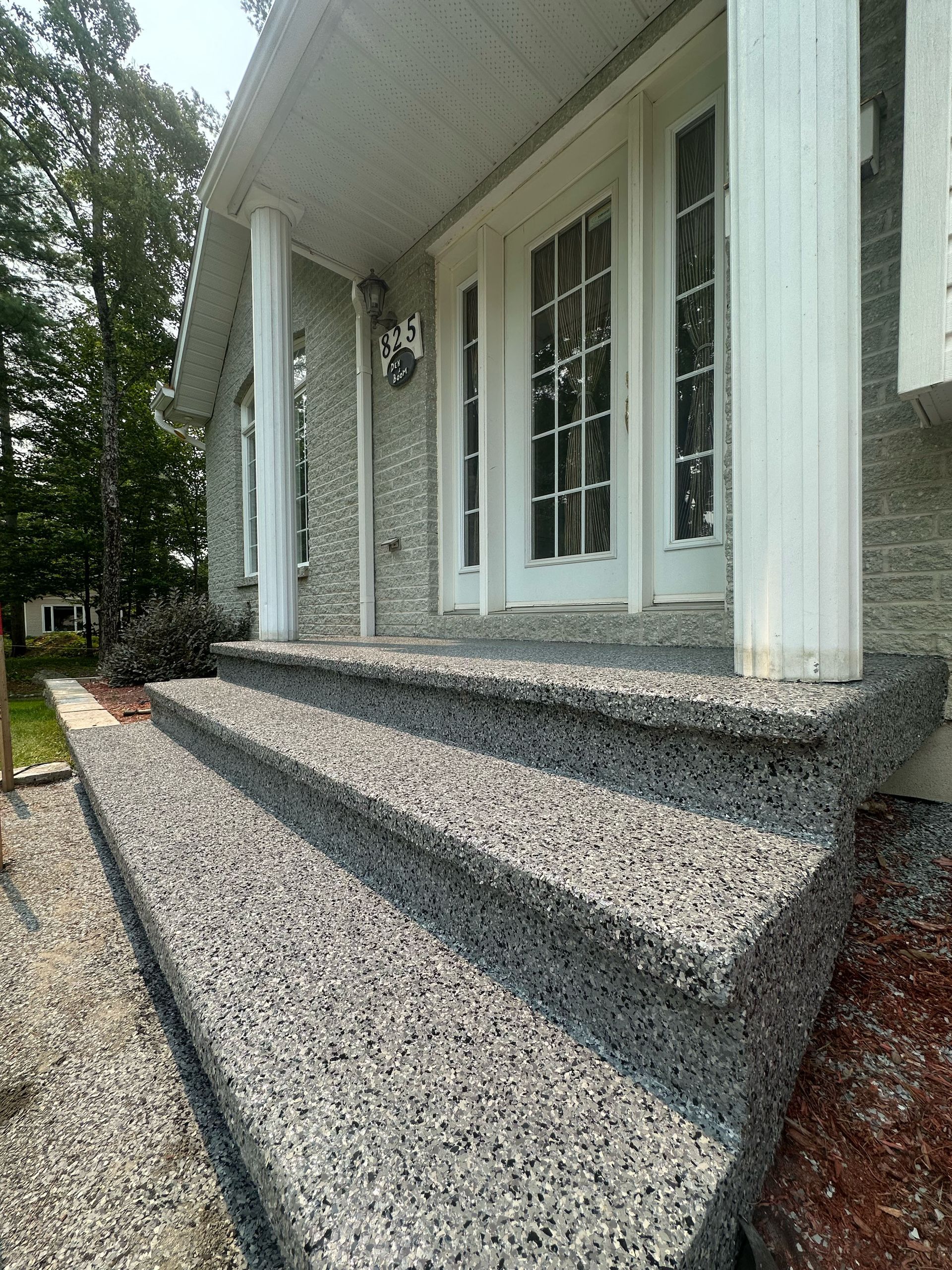 Gravel-textured front steps leading to a white house porch with double doors and columns
