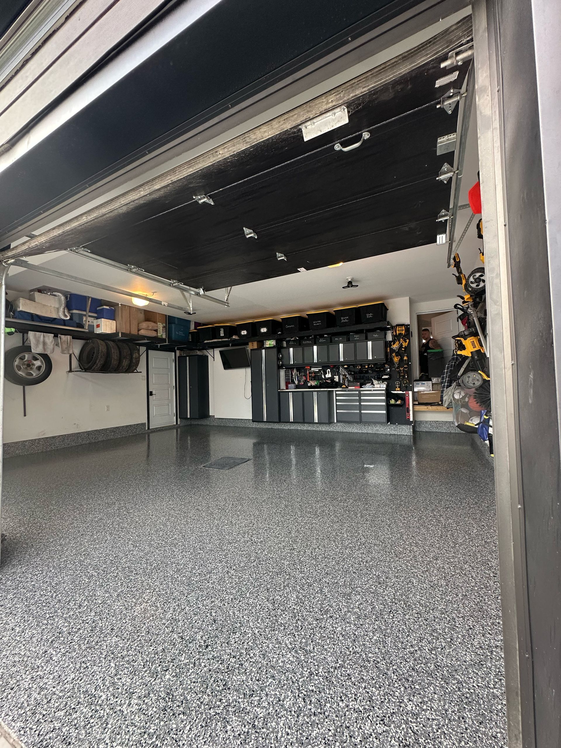 Empty garage with speckled epoxy floor, open black overhead door, and storage cabinets at the back.