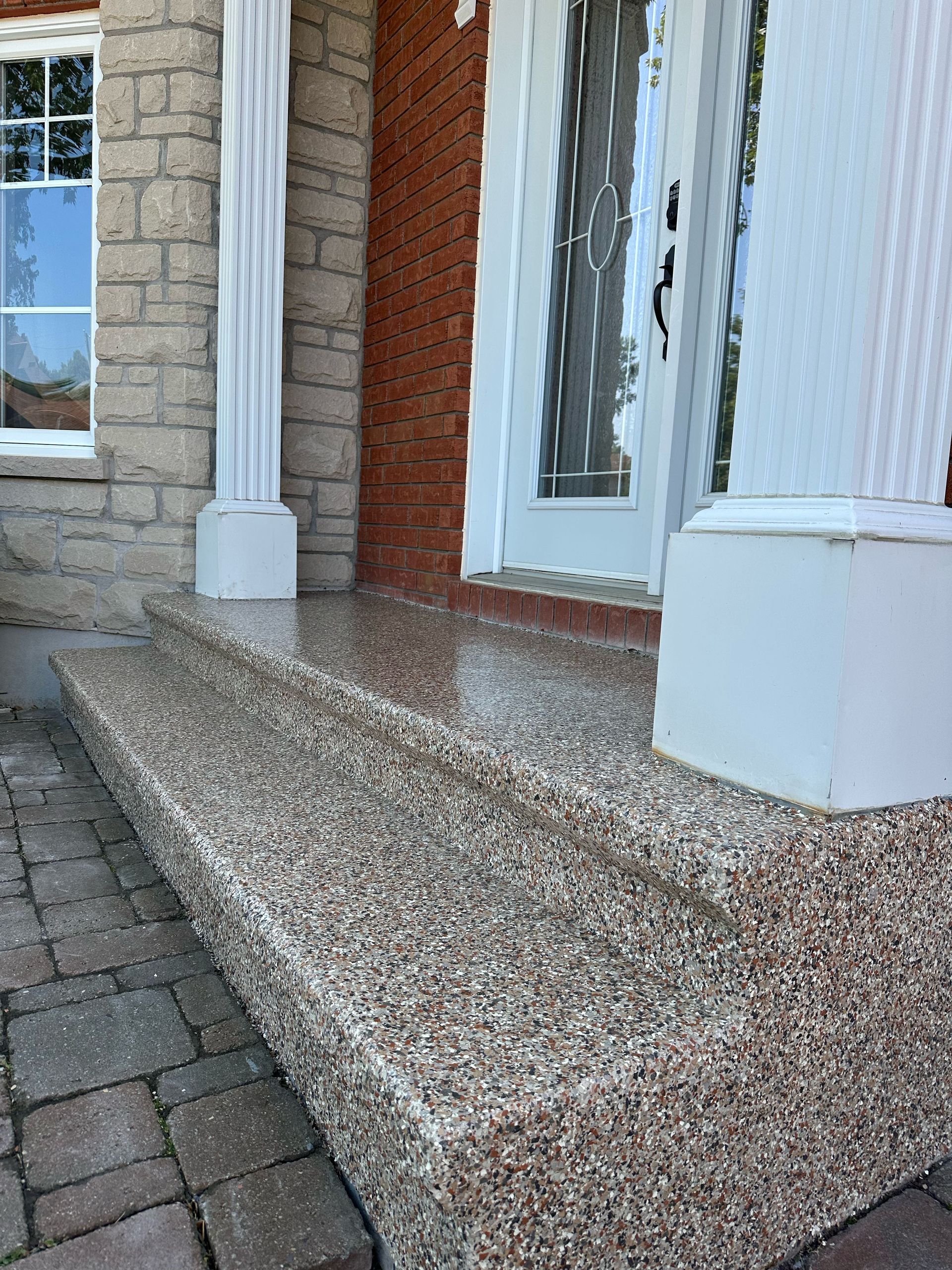 Front porch with pebble-finish steps, white columns, and brick entryway beside a glass door.