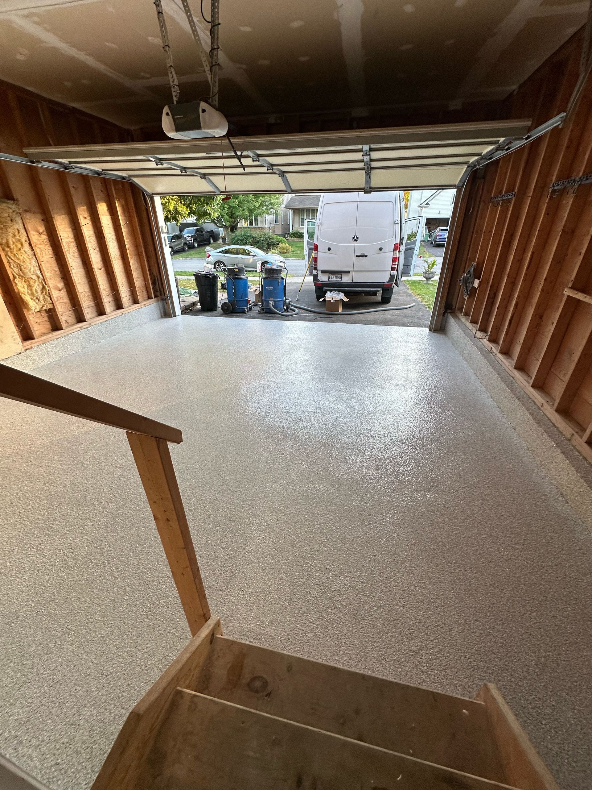 Interior view from a garage toward an open door, showing a white van and bins outside.
