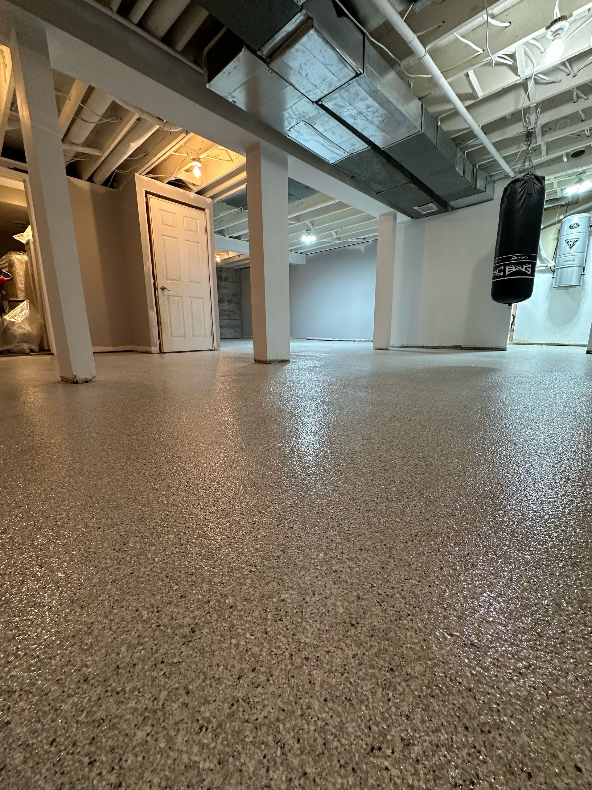 Empty interior with speckled floor, white columns, exposed ceiling beams, and a hanging punching bag.
