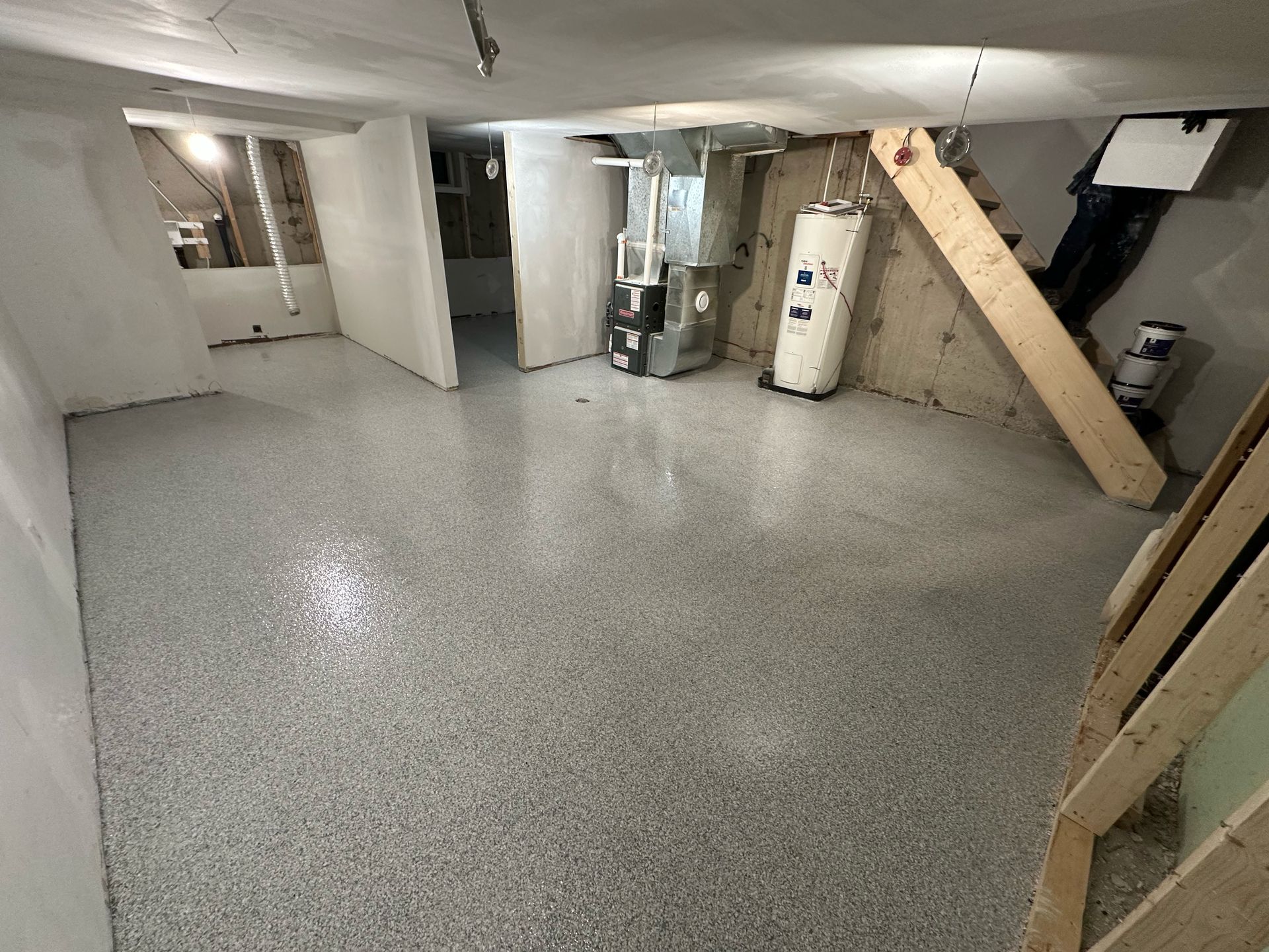 Basement utility room with speckled gray floor, water heater, furnace, and wooden stairs.