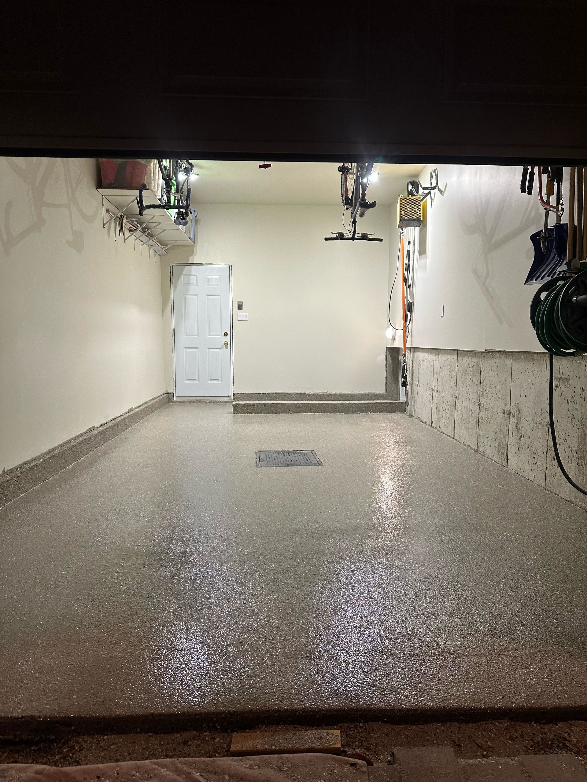 Empty garage with a wet concrete floor, white walls, and a closed white door.
