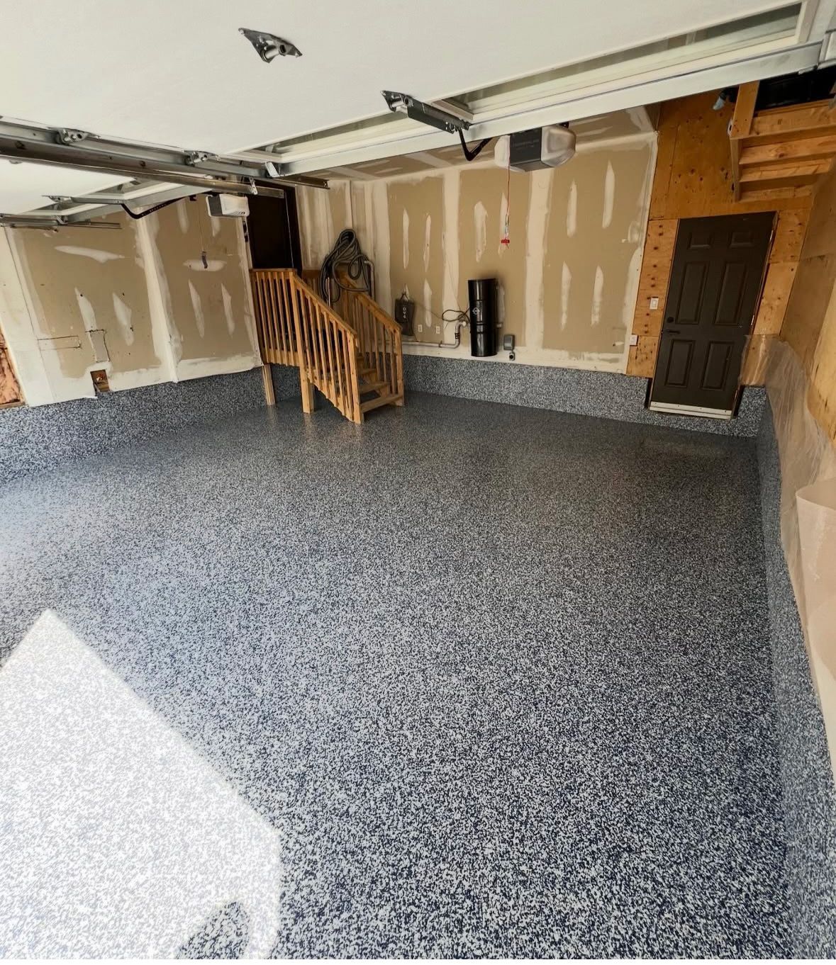 Spacious garage with gray speckled floor, unfinished walls, wooden stairs, and an open doorway