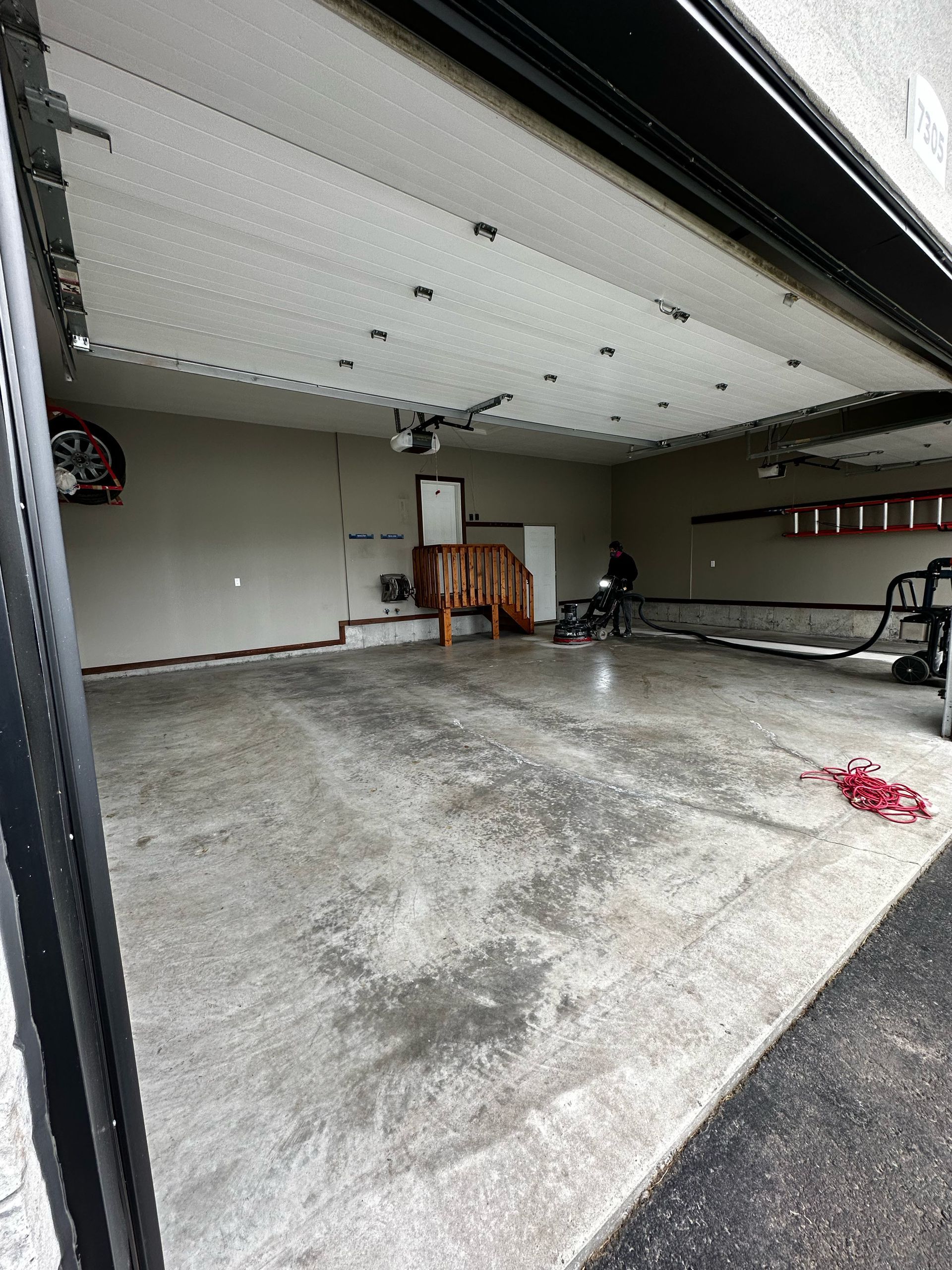 Garage vide avec sol en béton mouillé, porte de garage ouverte et vélo le long du mur de droite.