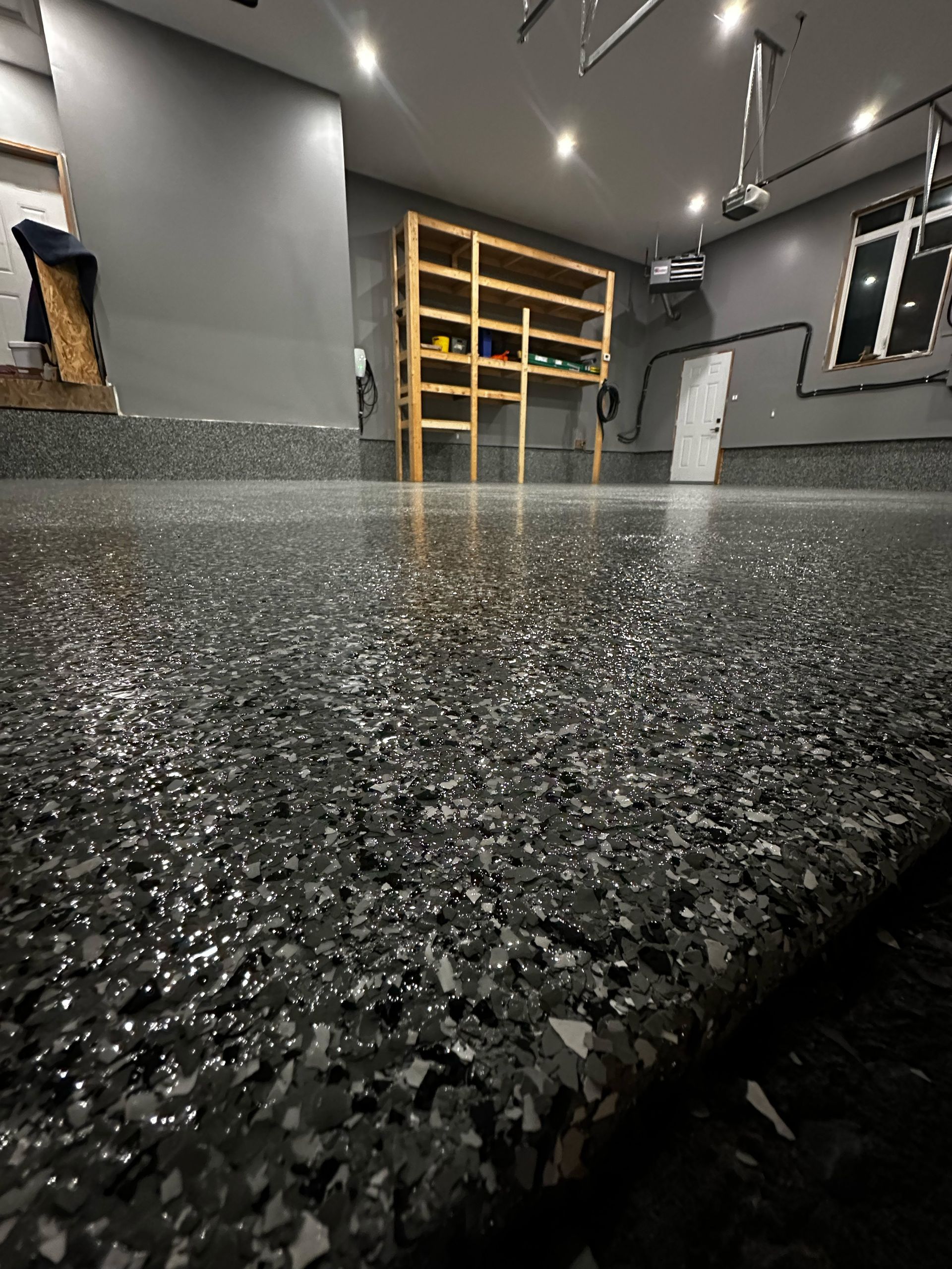Modern kitchen with a black speckled countertop, gray walls, and open shelving under ceiling lights
