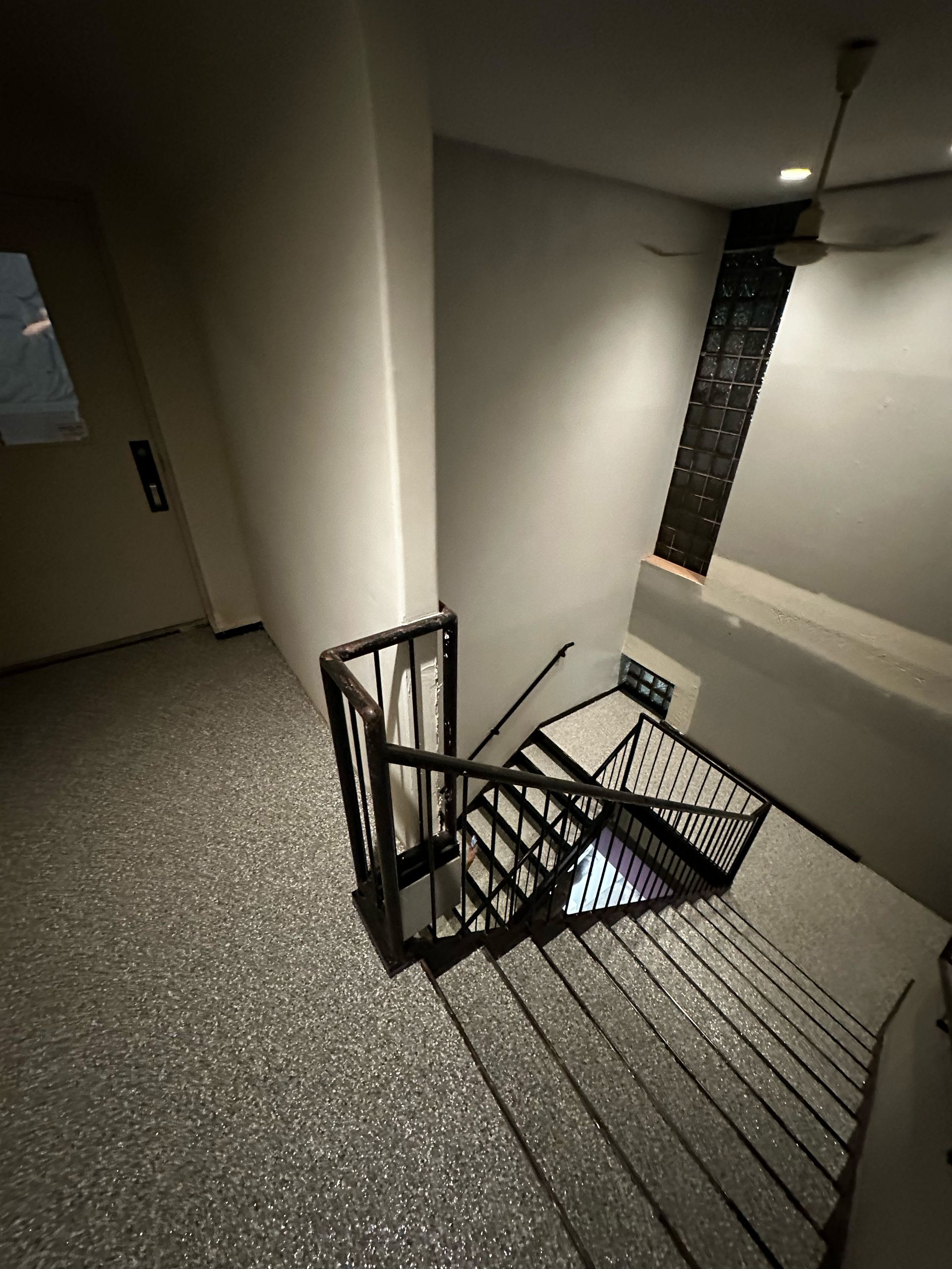 Indoor stairwell with black metal railing, gray floor, and a window at the landing.