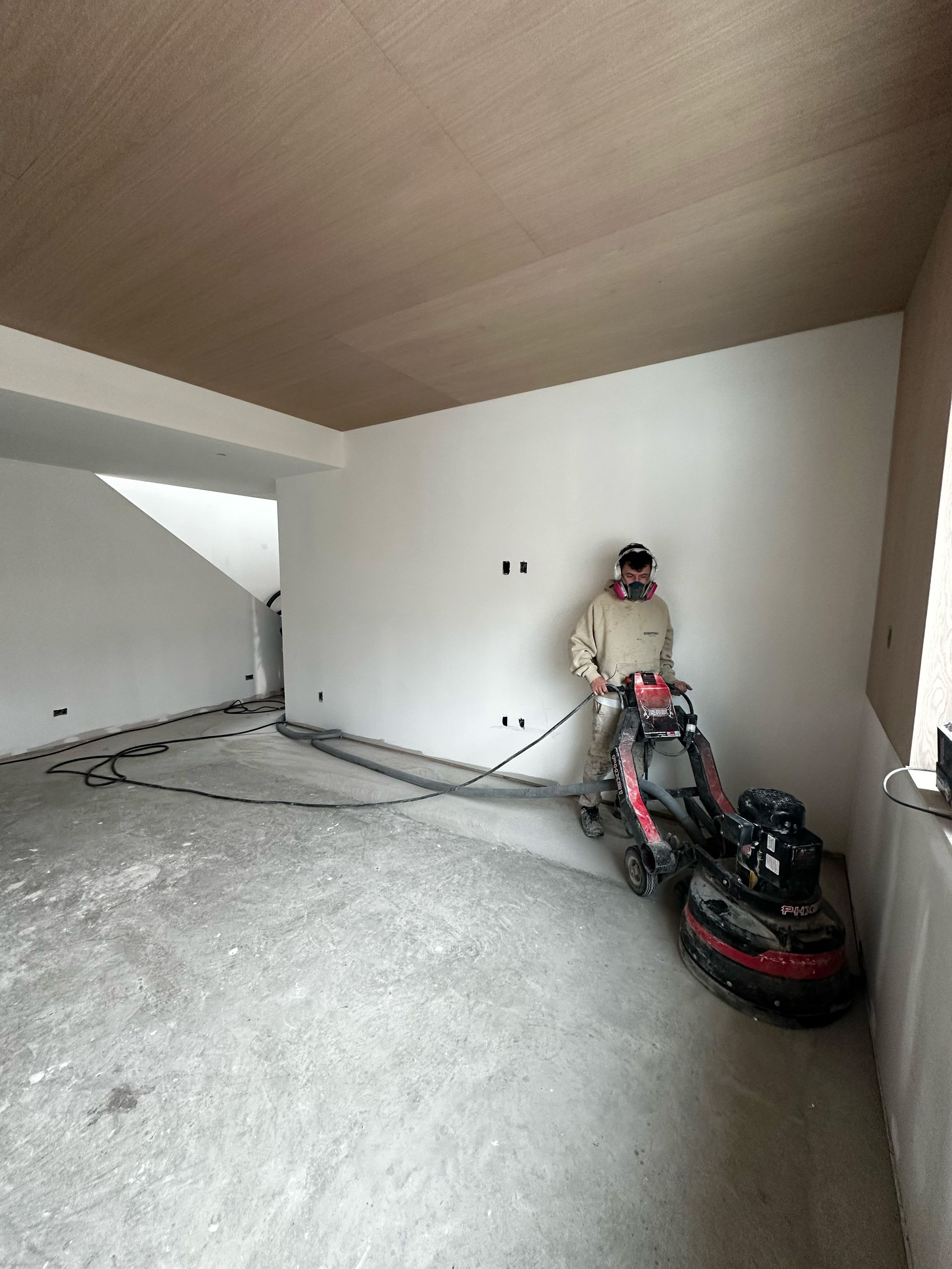 Pièce vide avec plafond en bois incliné, sol en béton et une moto rouge garée contre le mur.