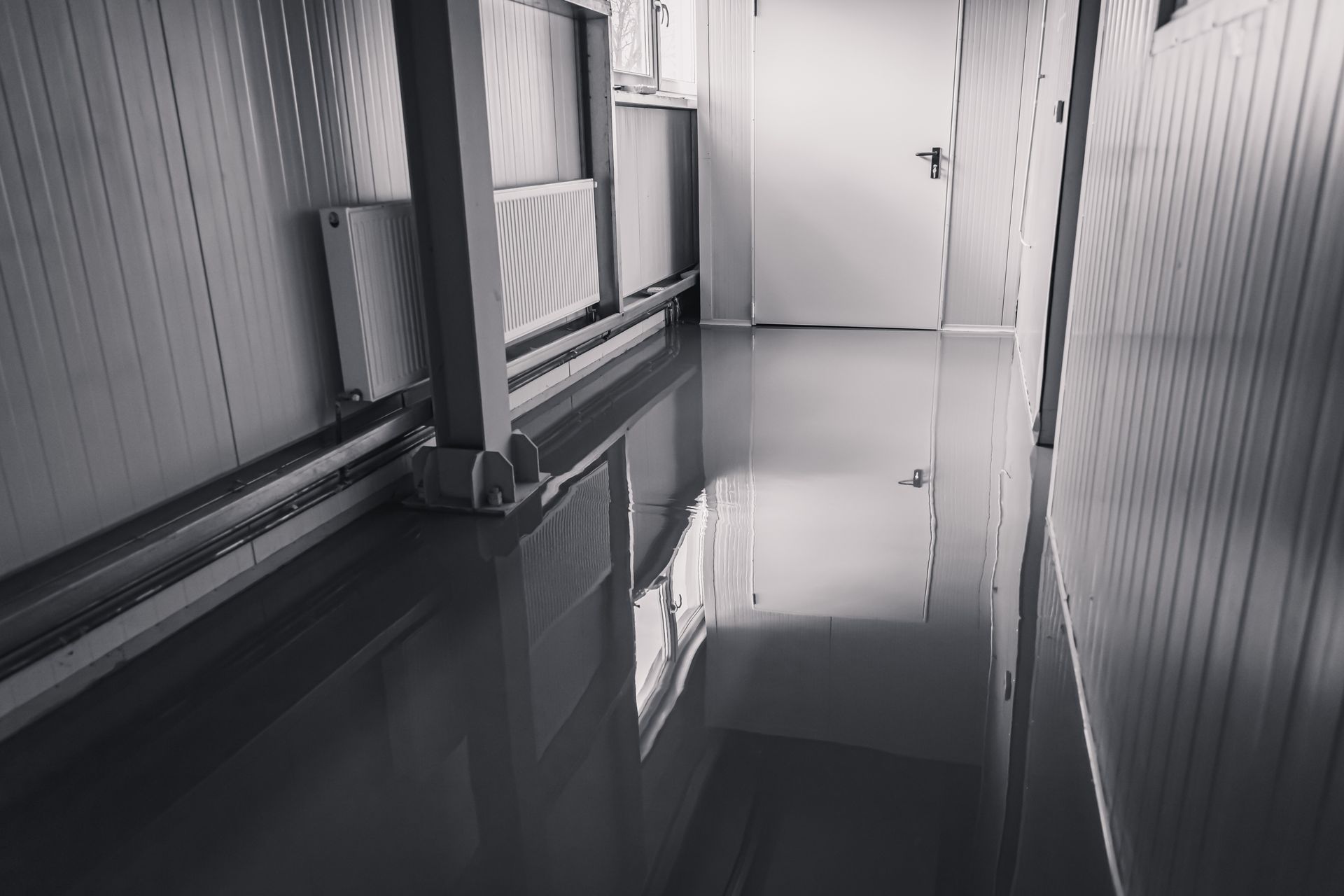 A black and white photo of a hallway with a reflection of a door in the floor.