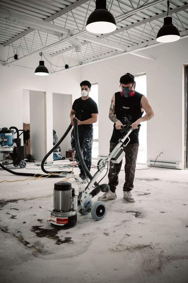 Two men wearing masks are cleaning a floor with a machine.