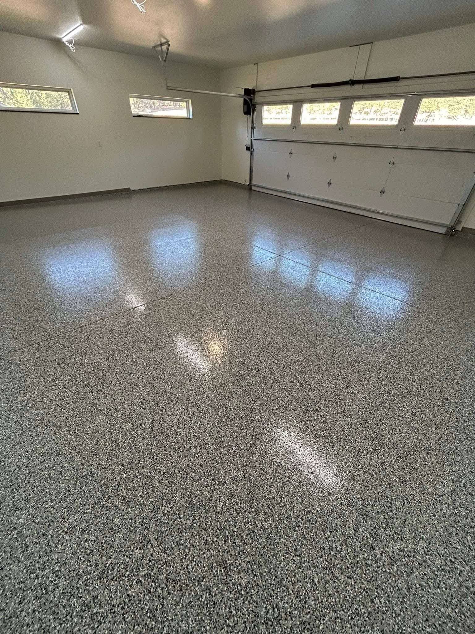 Empty garage with speckled epoxy floor, white walls, and high windows letting in light.