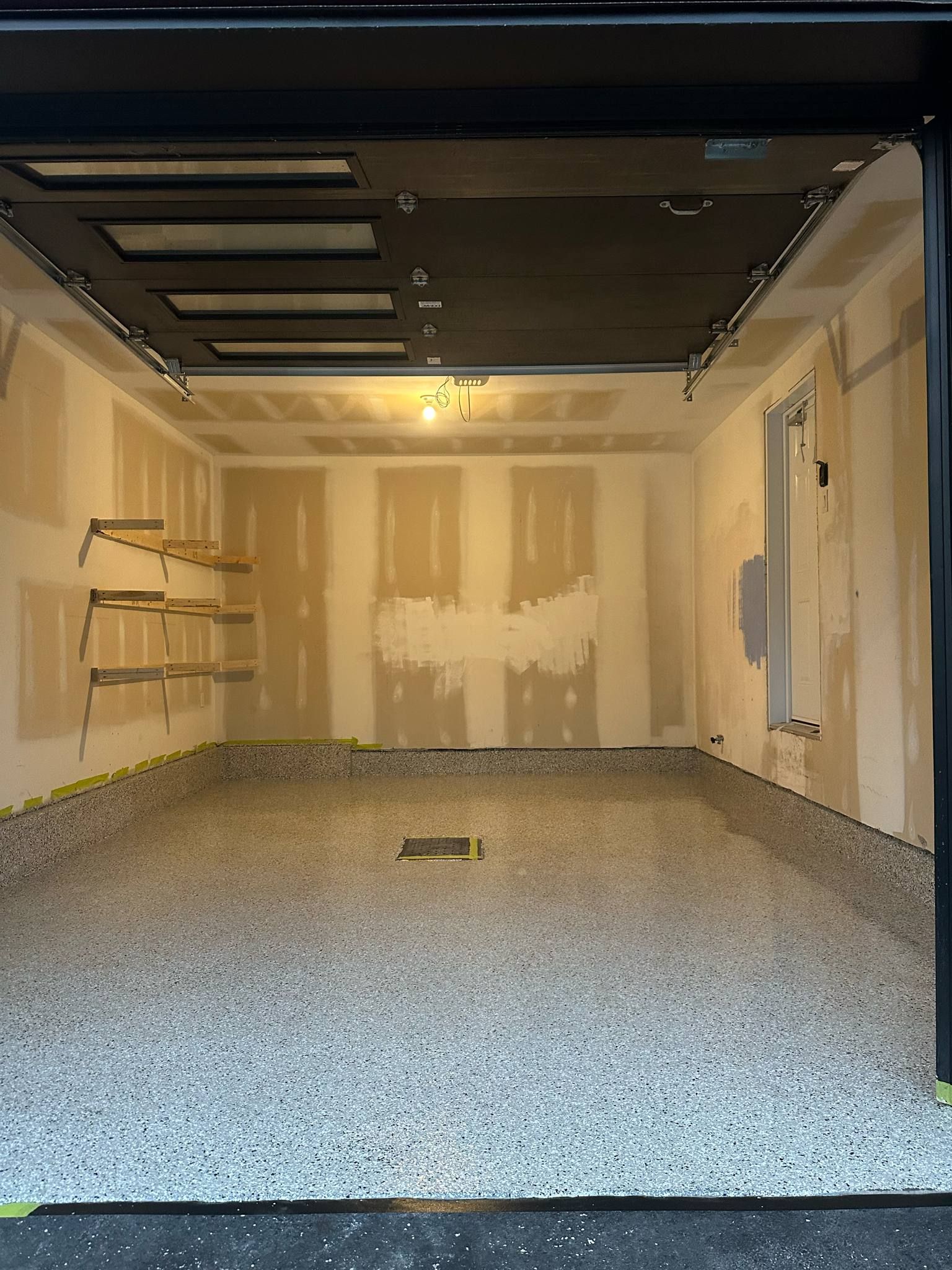 Empty garage with speckled floor, exposed ceiling, and unfinished drywall walls.
