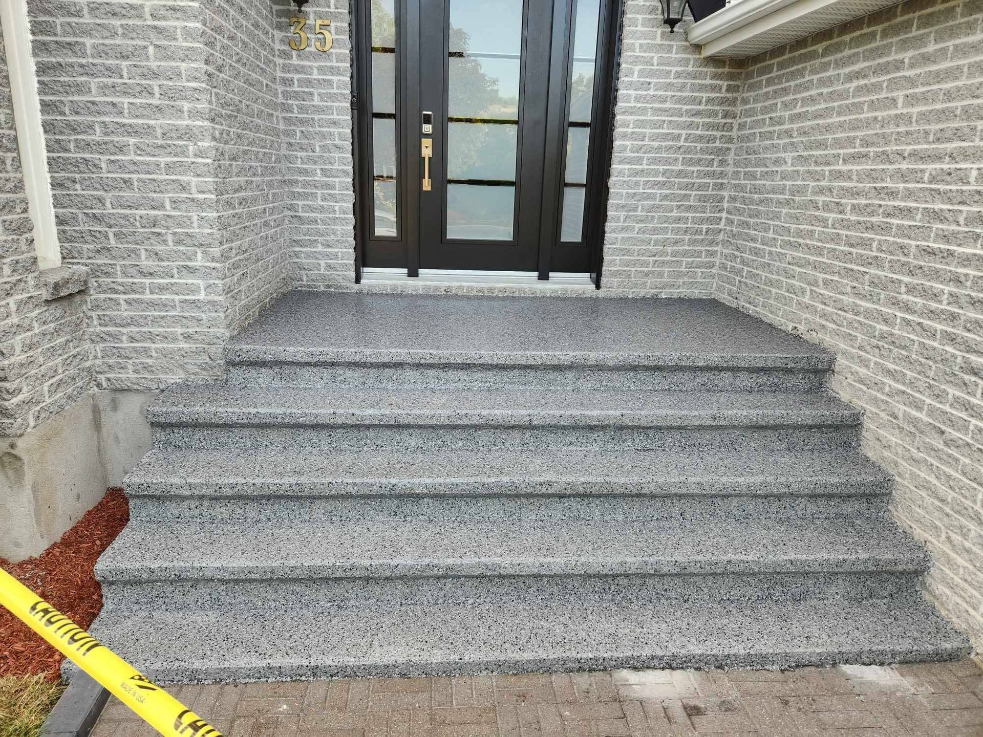 Granite front steps leading to a black glass door between brick walls