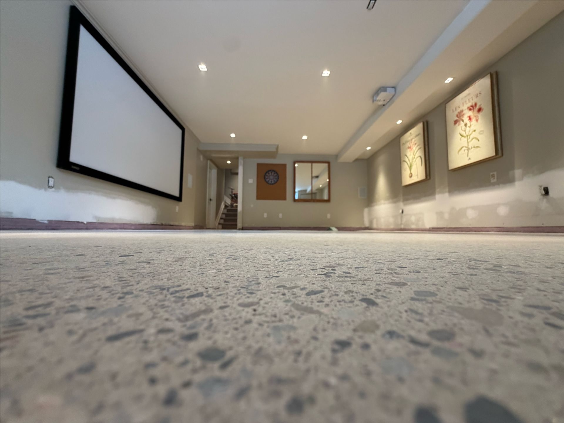 Galerie moderne avec un grand écran de projection, des œuvres encadrées sur des murs beiges et un sol recouvert de moquette, vue d'en bas.