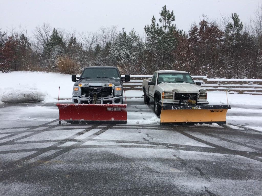 Two snow plows are parked next to each other in a parking lot.