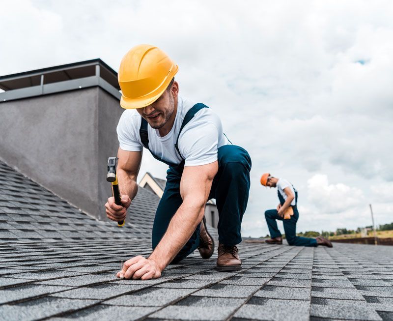 Two construction workers are working on a roof.