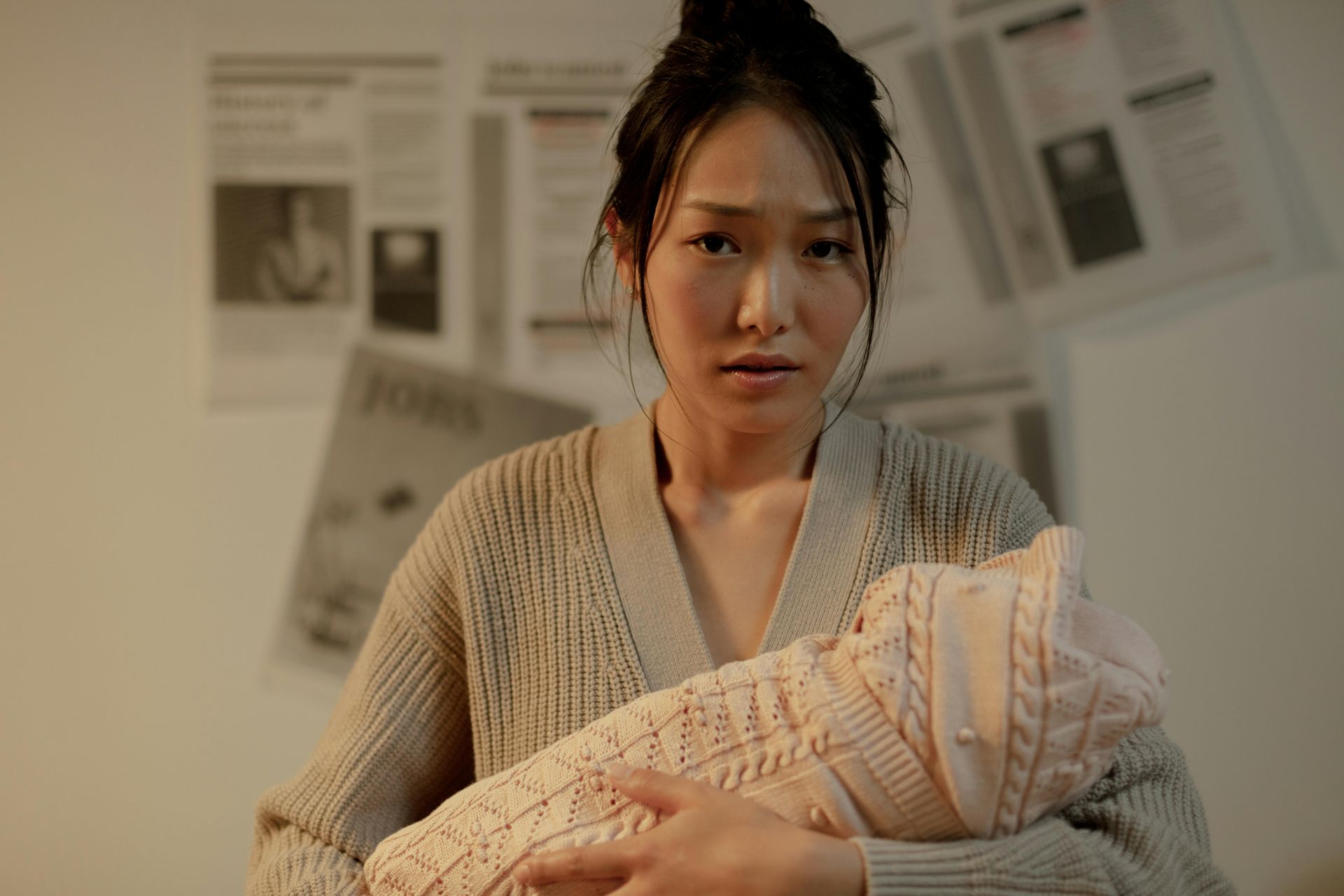 Woman holding a swaddled baby in a softly lit room with papers pinned on the wall