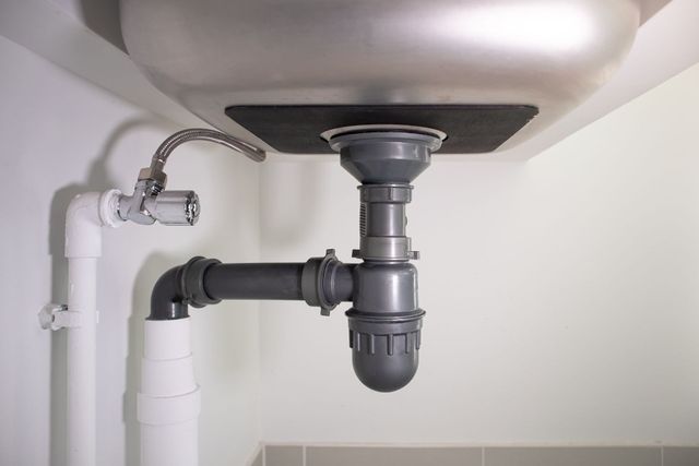Under-sink plumbing with drainpipe, P-trap, and white water supply lines under a bathroom sink