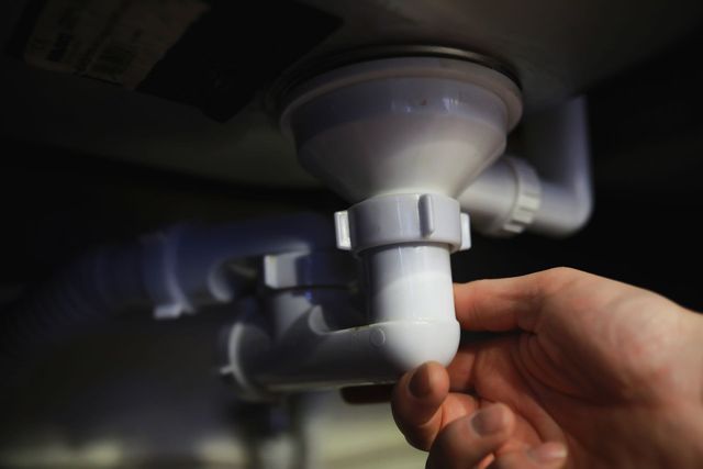 Hand turning a white plastic sink drain pipe under a bathroom sink