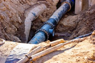 Blue water pipe being repaired in a dirt trench with tools nearby