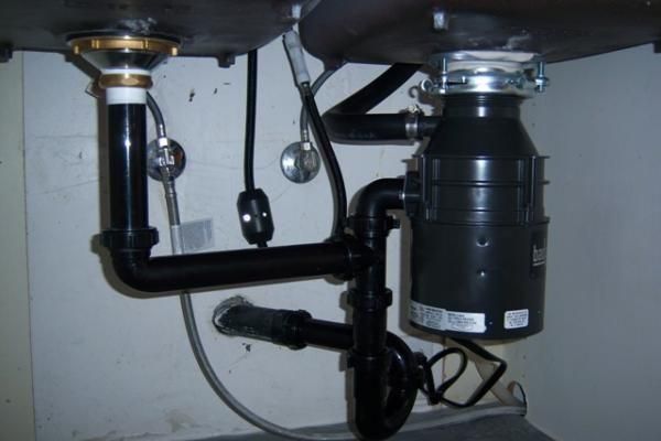 Under-sink plumbing with black drain pipes and a garbage disposal unit
