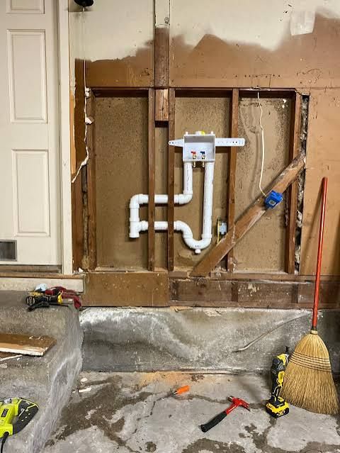 Kitchen wall opened for plumbing repair with exposed pipes and tools on the floor