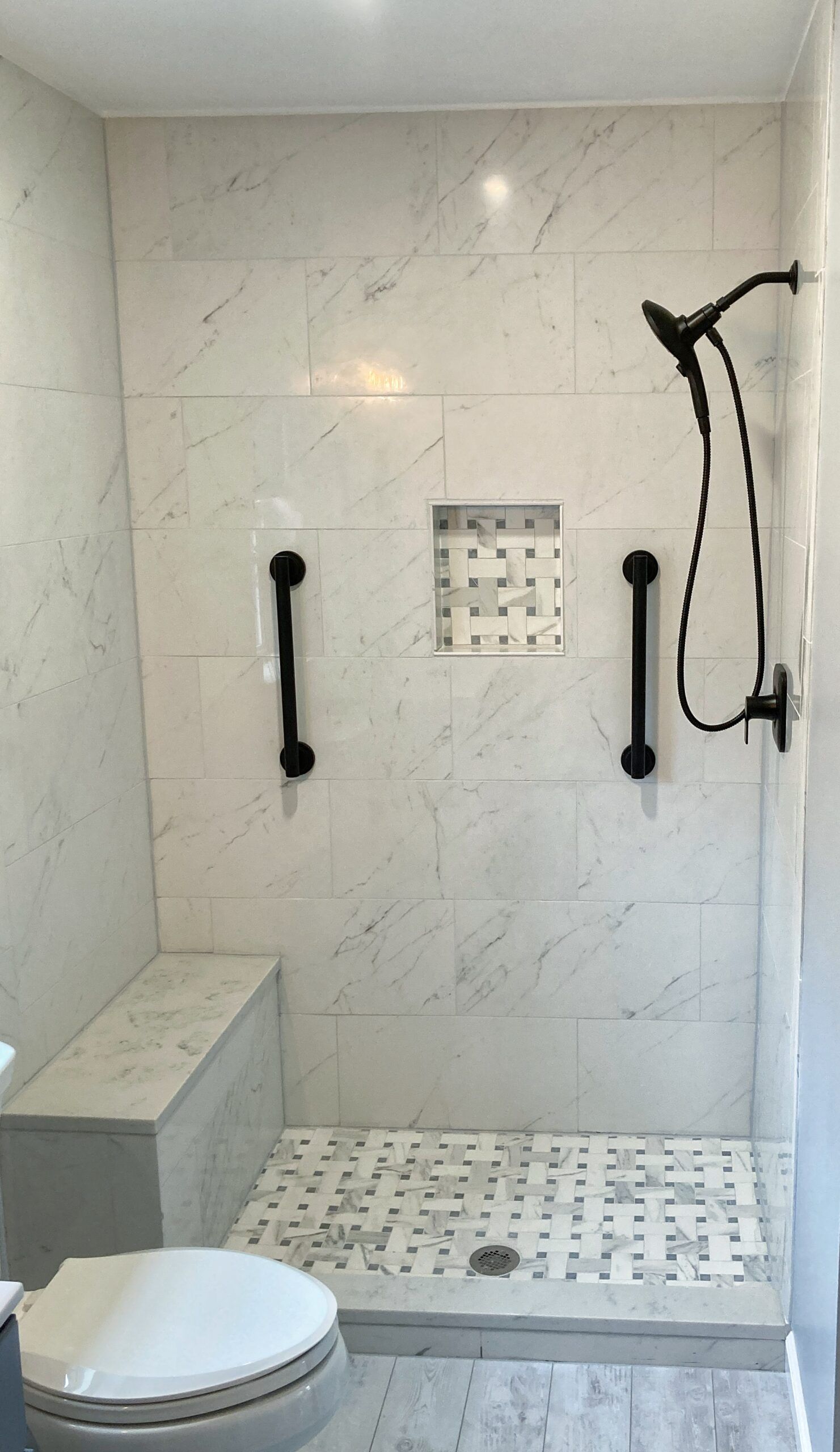 Accessible marble-tiled shower room with grab bars, bench, handheld shower, and shower chair.