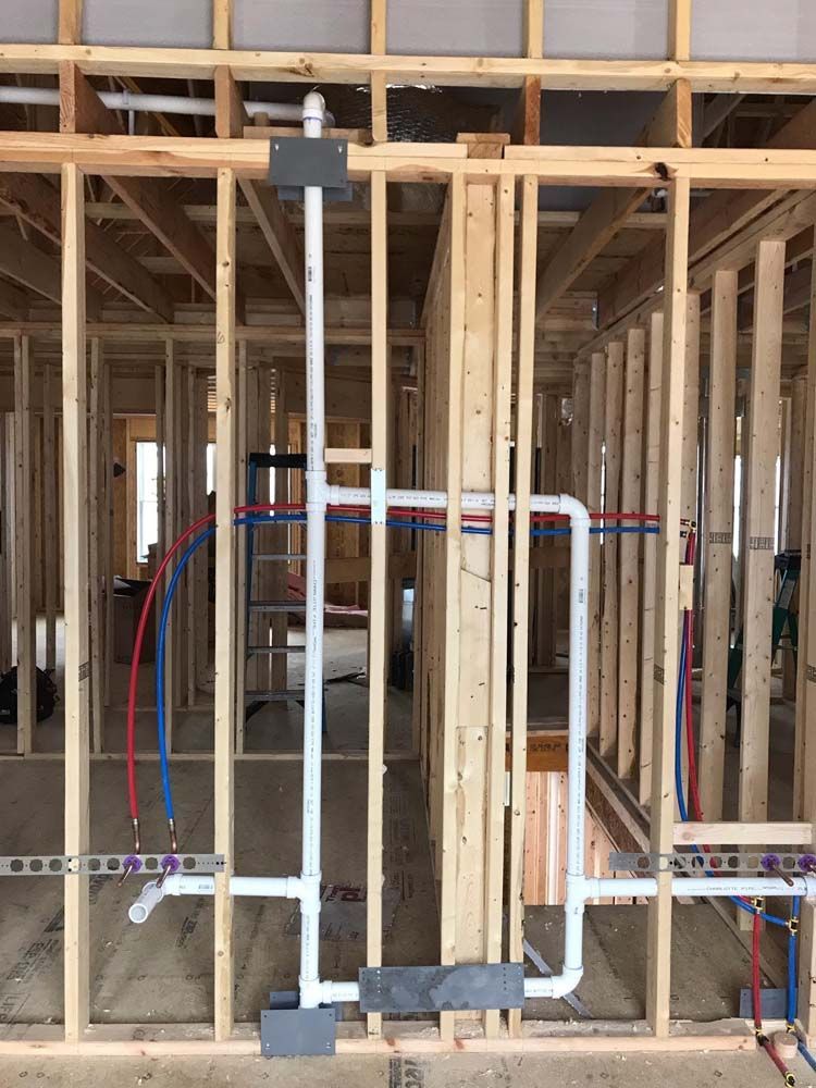 Framed construction wall with exposed studs, plumbing pipes, and electrical wiring inside an unfinished room