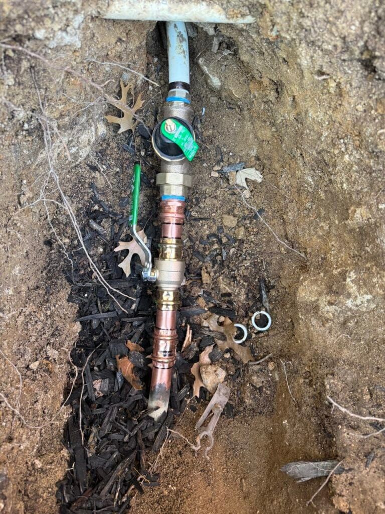 Exposed copper pipe and shutoff valve in a dirt trench beneath ground surface