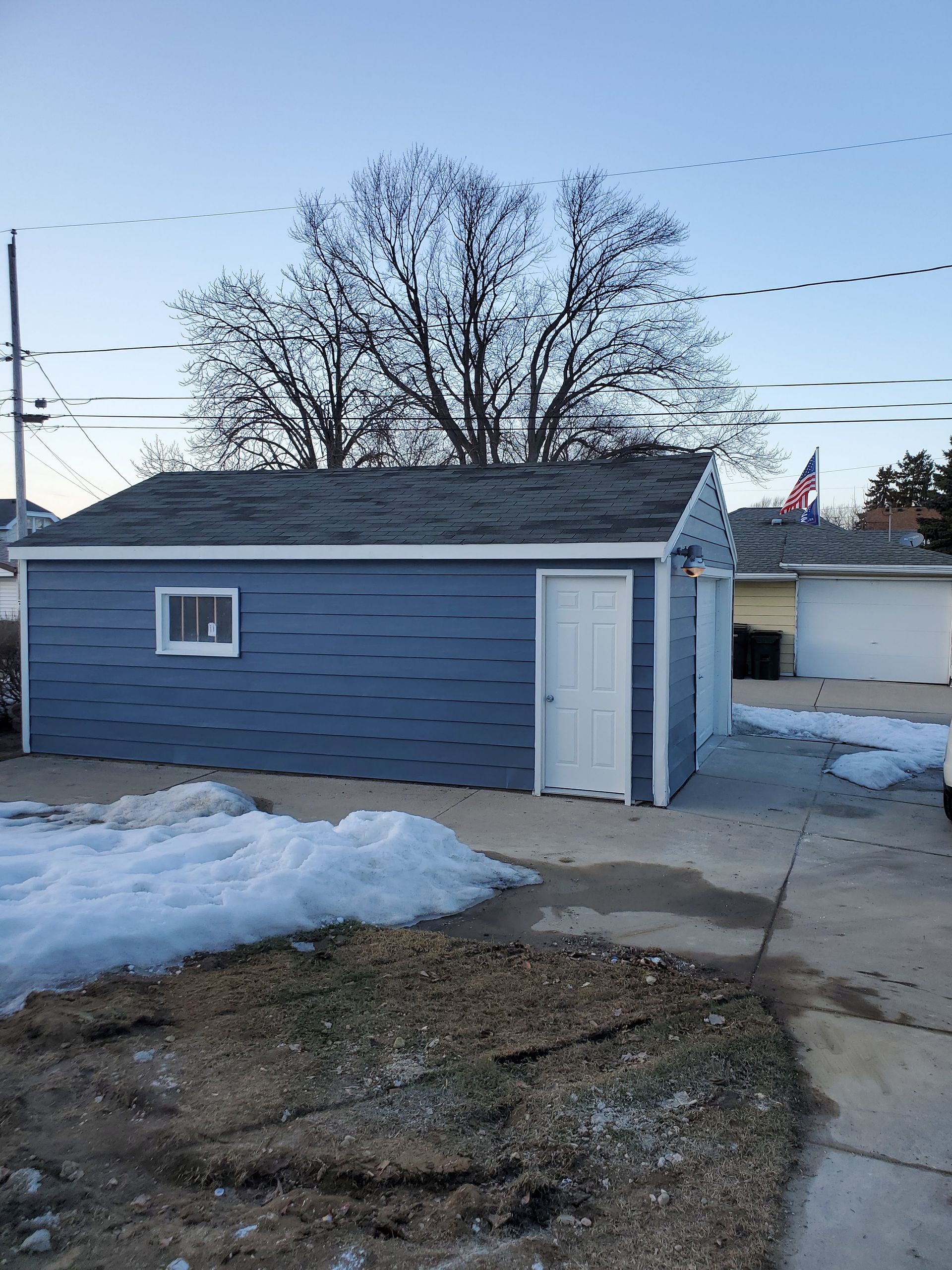 a blue garage with a roof and a window is in the snow .