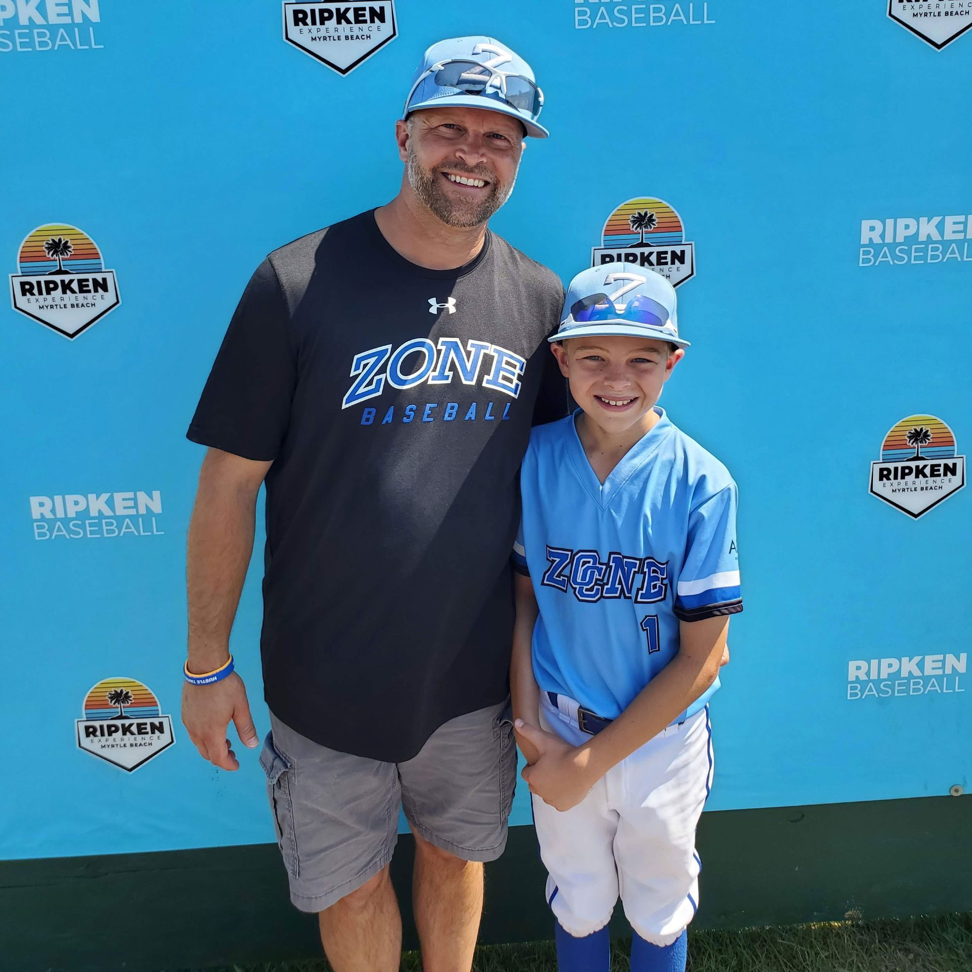 Advantage Matt Bruins  in a zone baseball shirt stands next to a boy in a blue jersey