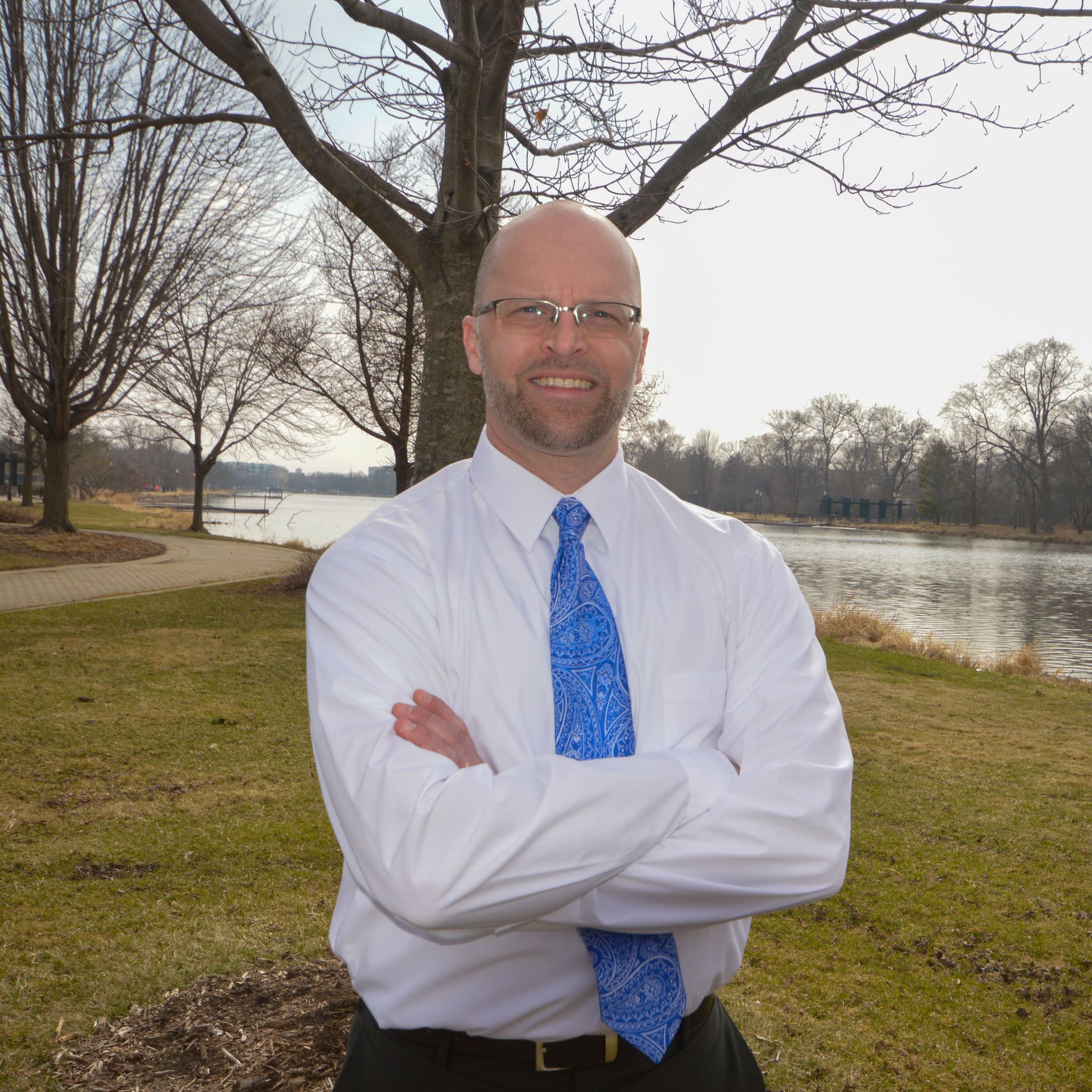 a man in a white shirt and blue tie stands with his arms crossed