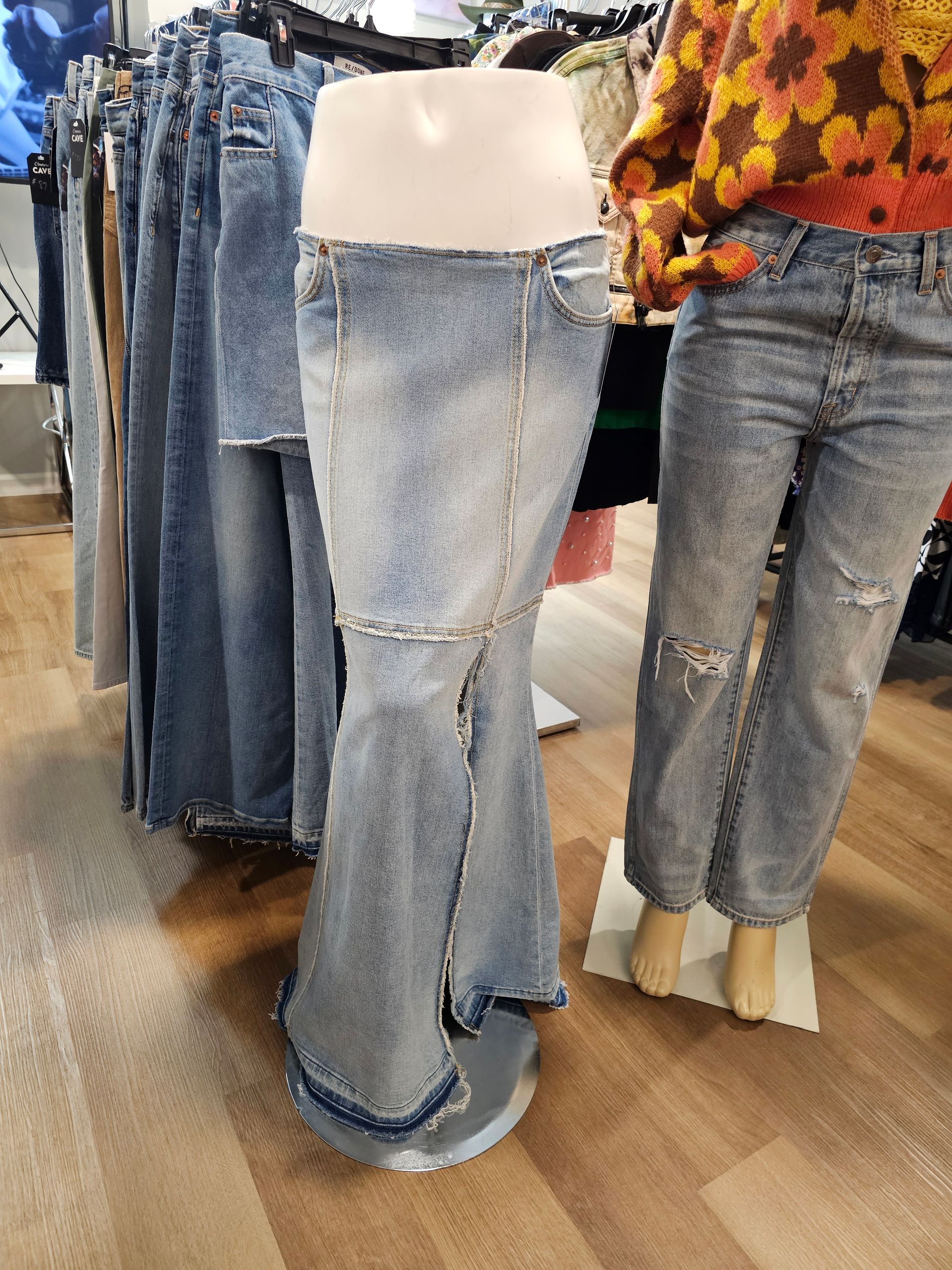 A clothing rack in a store displays a light-wash denim mermaid skirt on a mannequin next to other jeans.