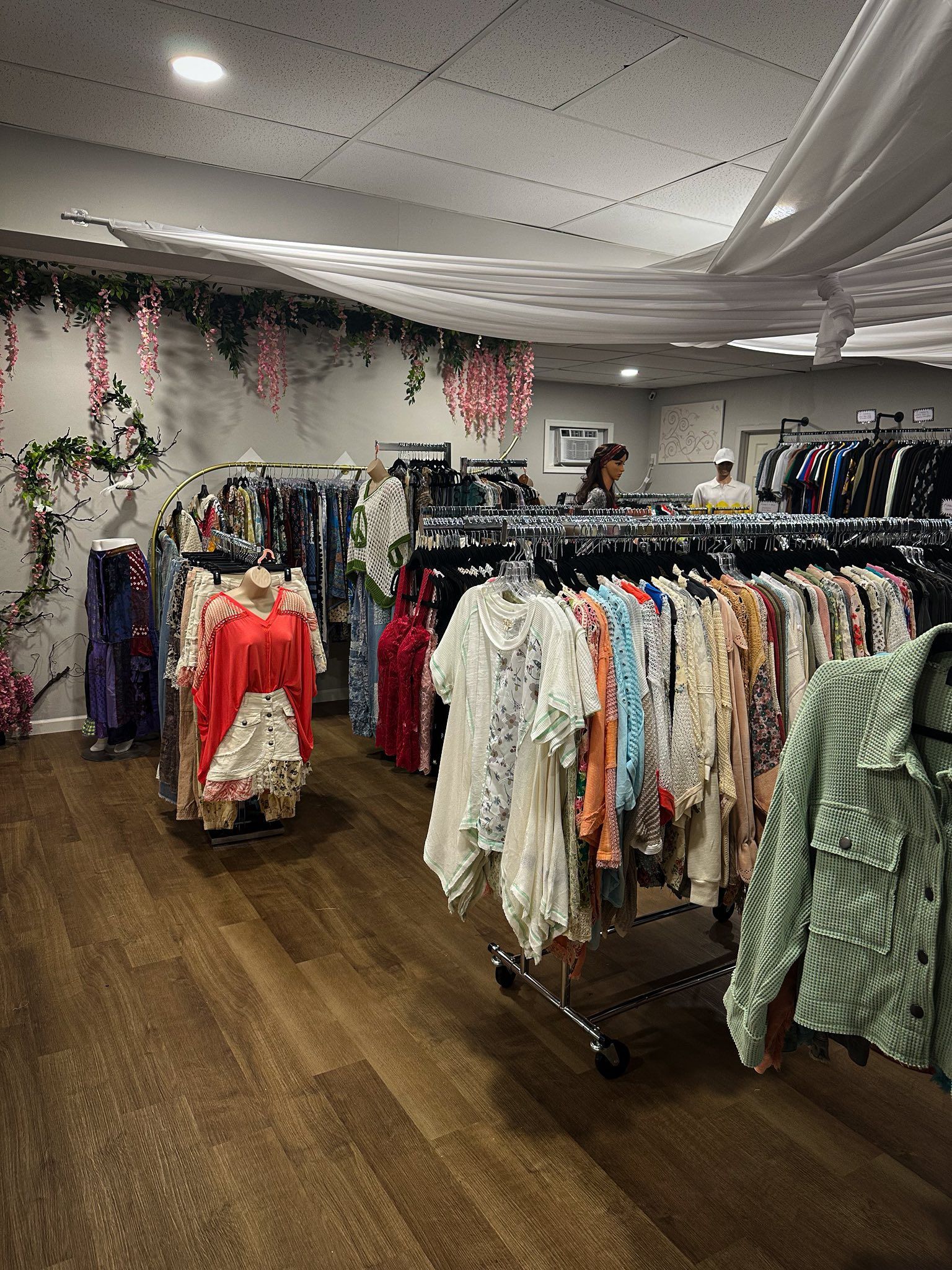 Clothing racks in a boutique with floral decor and a light wood floor.