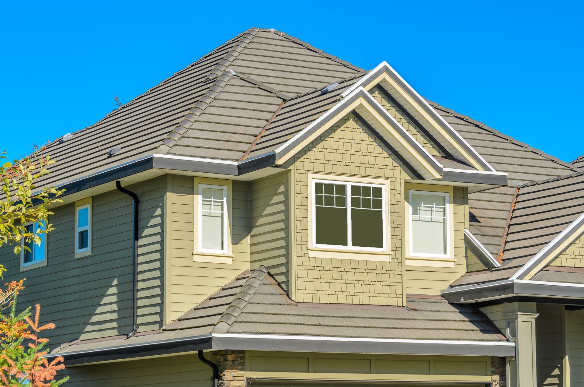 Modern beige house exterior with gray shingle roof and bright blue sky