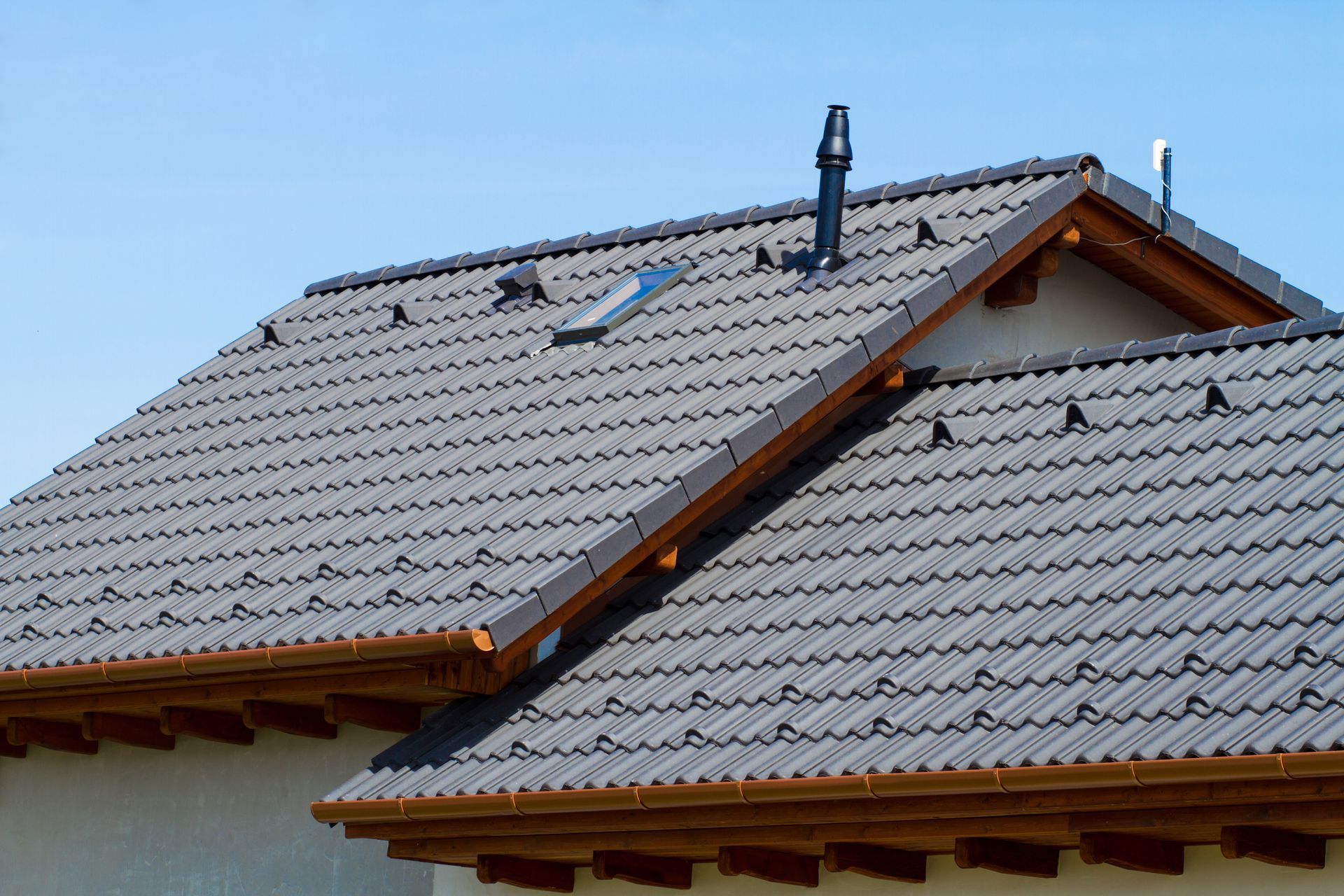 Gray tiled roofs with a skylight and chimney on a house under a clear blue sky