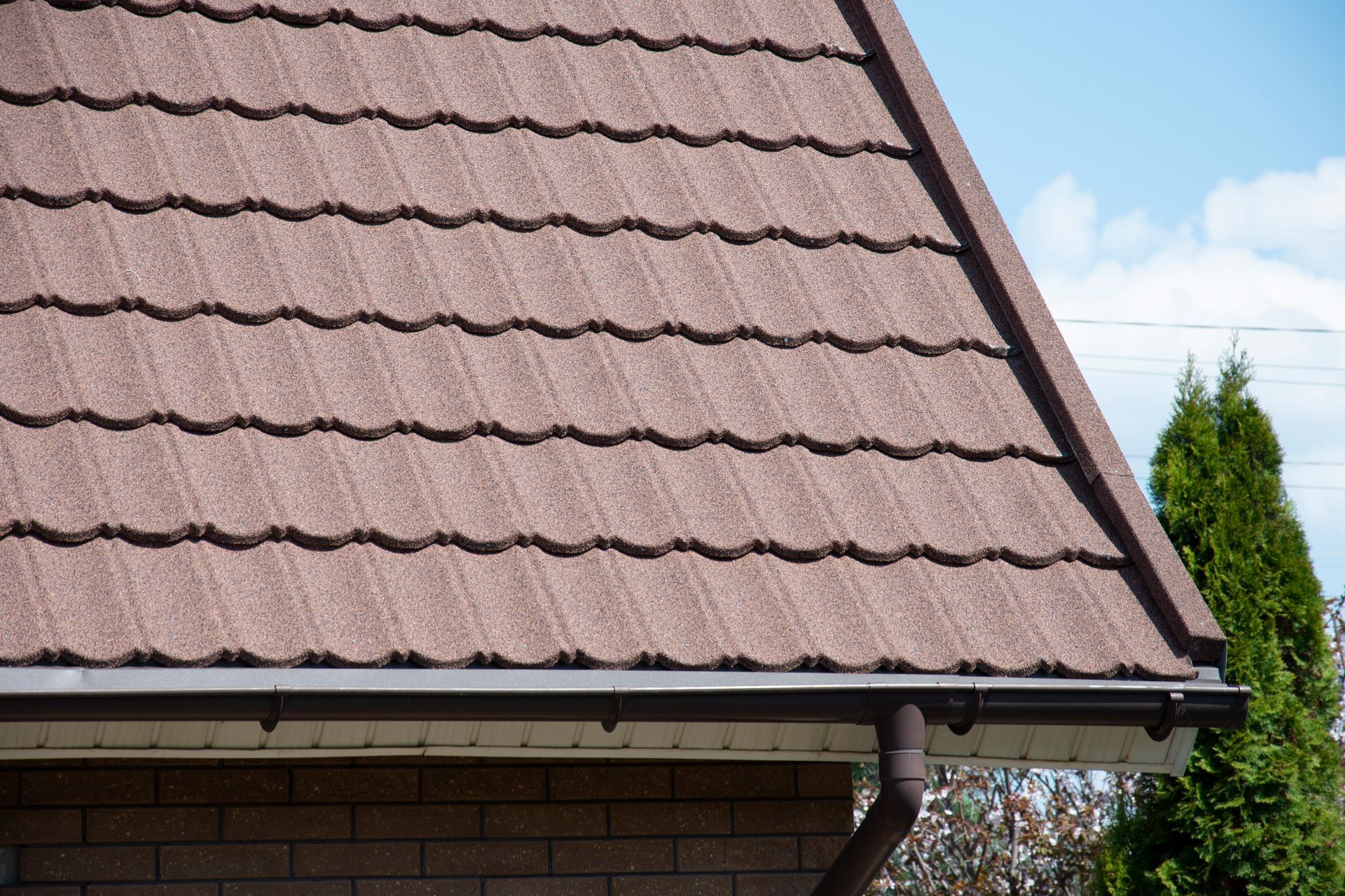 Brown tiled house roof with gutters against a blue sky