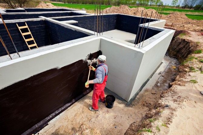 Worker painting basement wall in a concrete foundation under construction