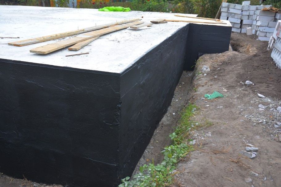 Black concrete foundation or retaining wall beside a dirt path, with wooden planks on top.