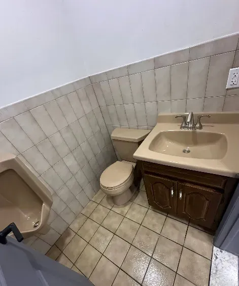 Bathroom with a urinal, toilet, and sink with a brown vanity. Beige and brown tones.