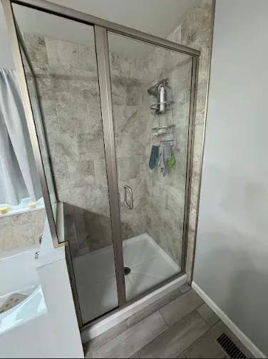 Shower with sliding glass doors, gray tiled walls, and a white shower basin.