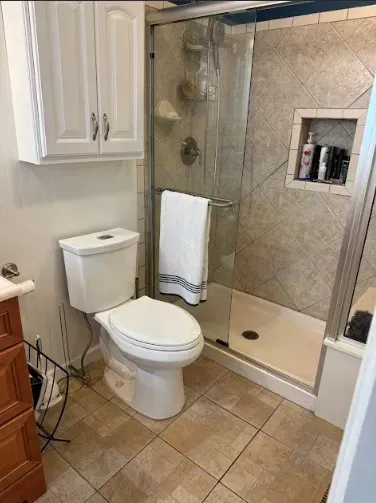 Bathroom with toilet, shower with glass door, cabinets, and tiled floor.